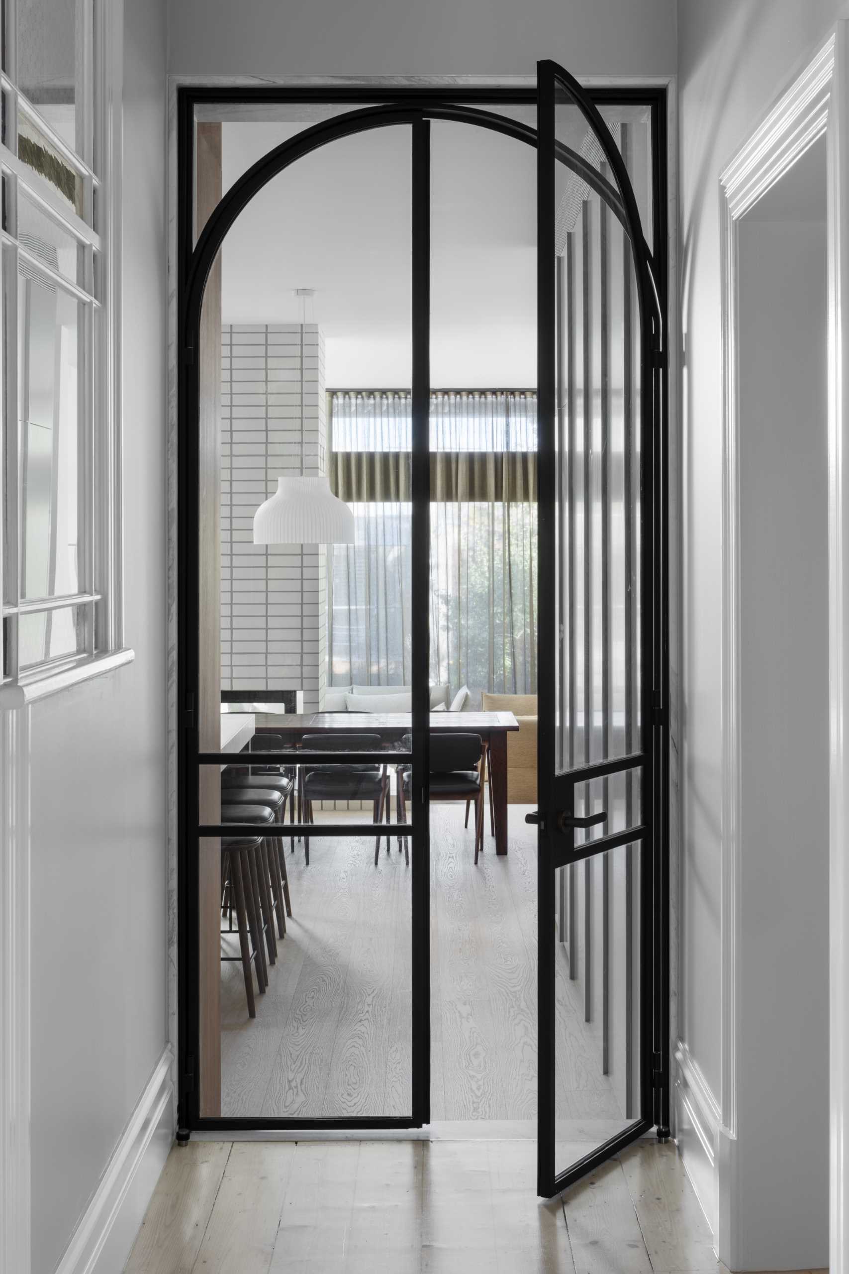 A black-framed arched door connects the original parts of the home with the new addition.