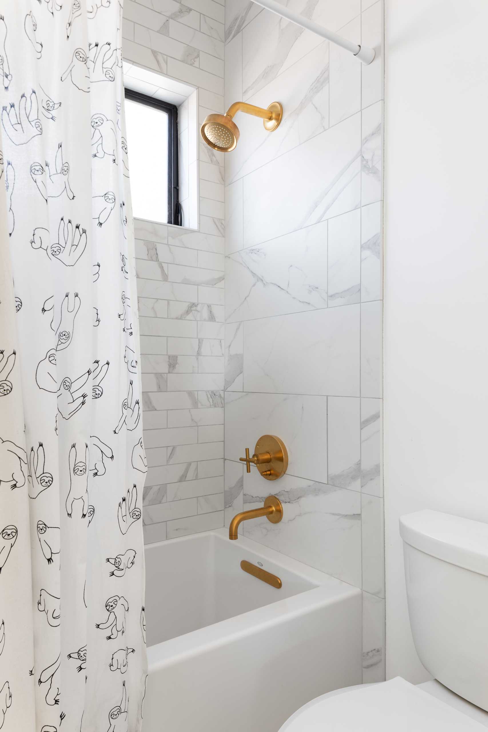 A modern bathroom with a combination bath and shower, with a shower curtain with sloth print adding a touch of fun.
