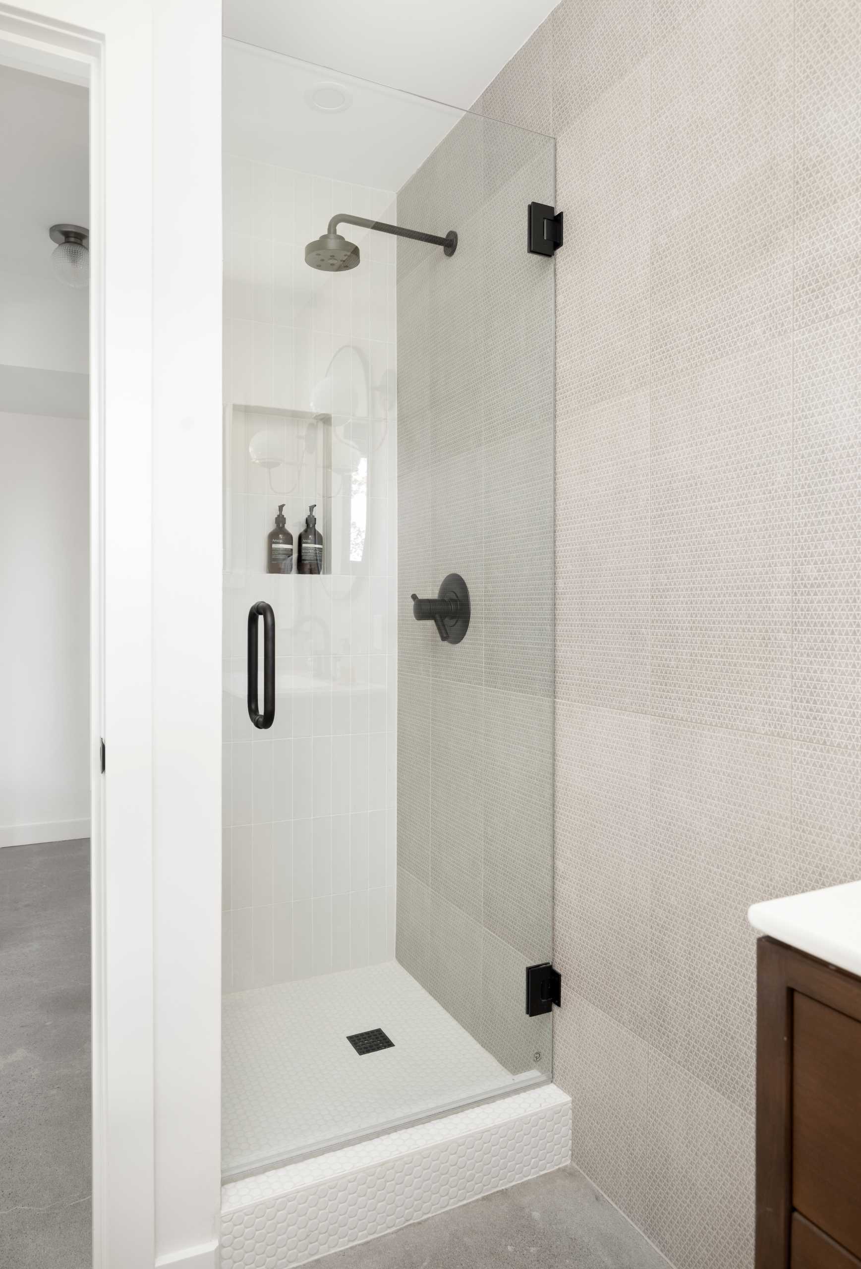 In this updated bathroom, a tiled wall creates a backdrop for the dark wood vanity, while a black-framed oval mirror complements the window frame.