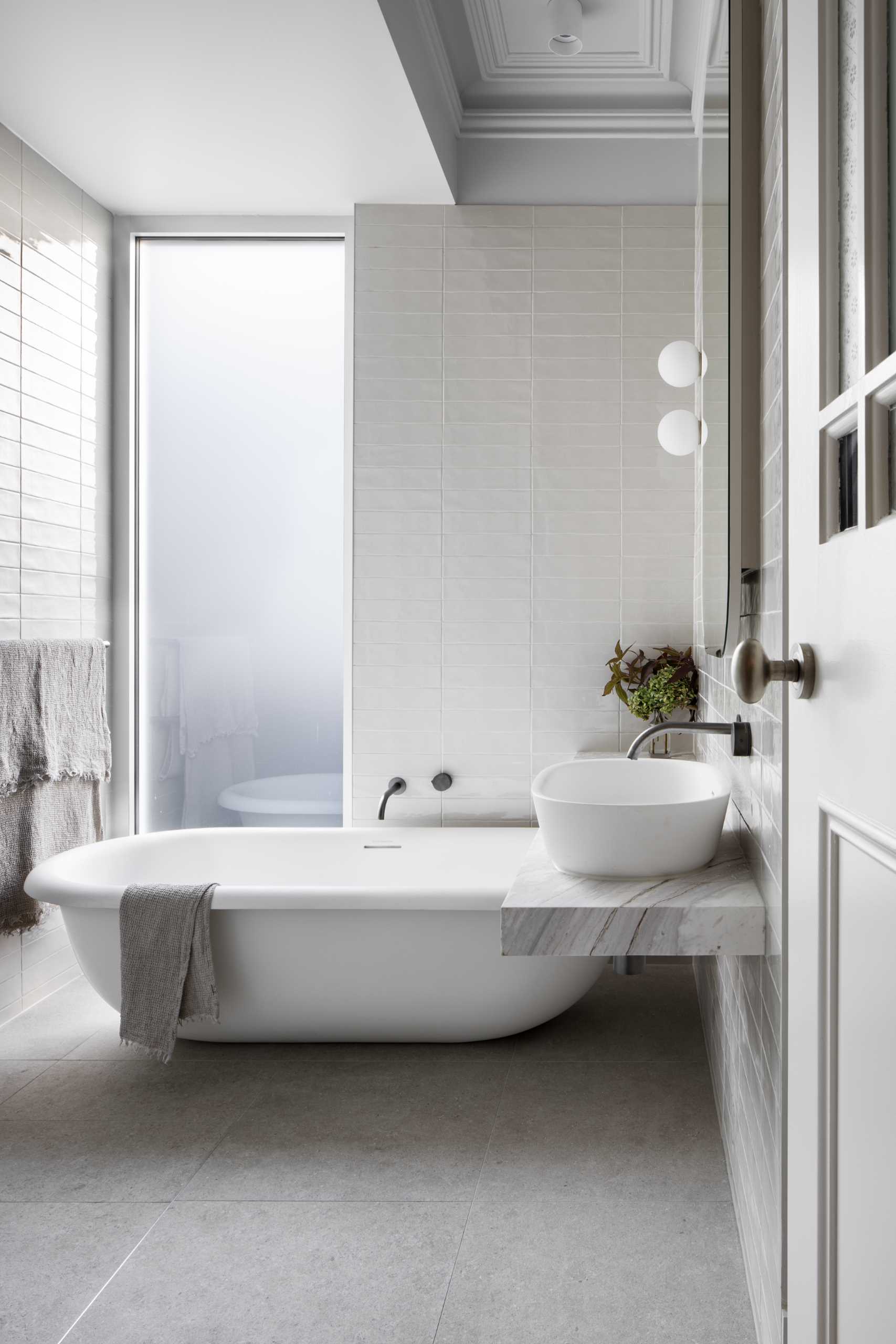 In this bathroom, there's a floating vanity and freestanding bathtub, while an opaque window provides privacy and at the same time, allows the light to filter through.