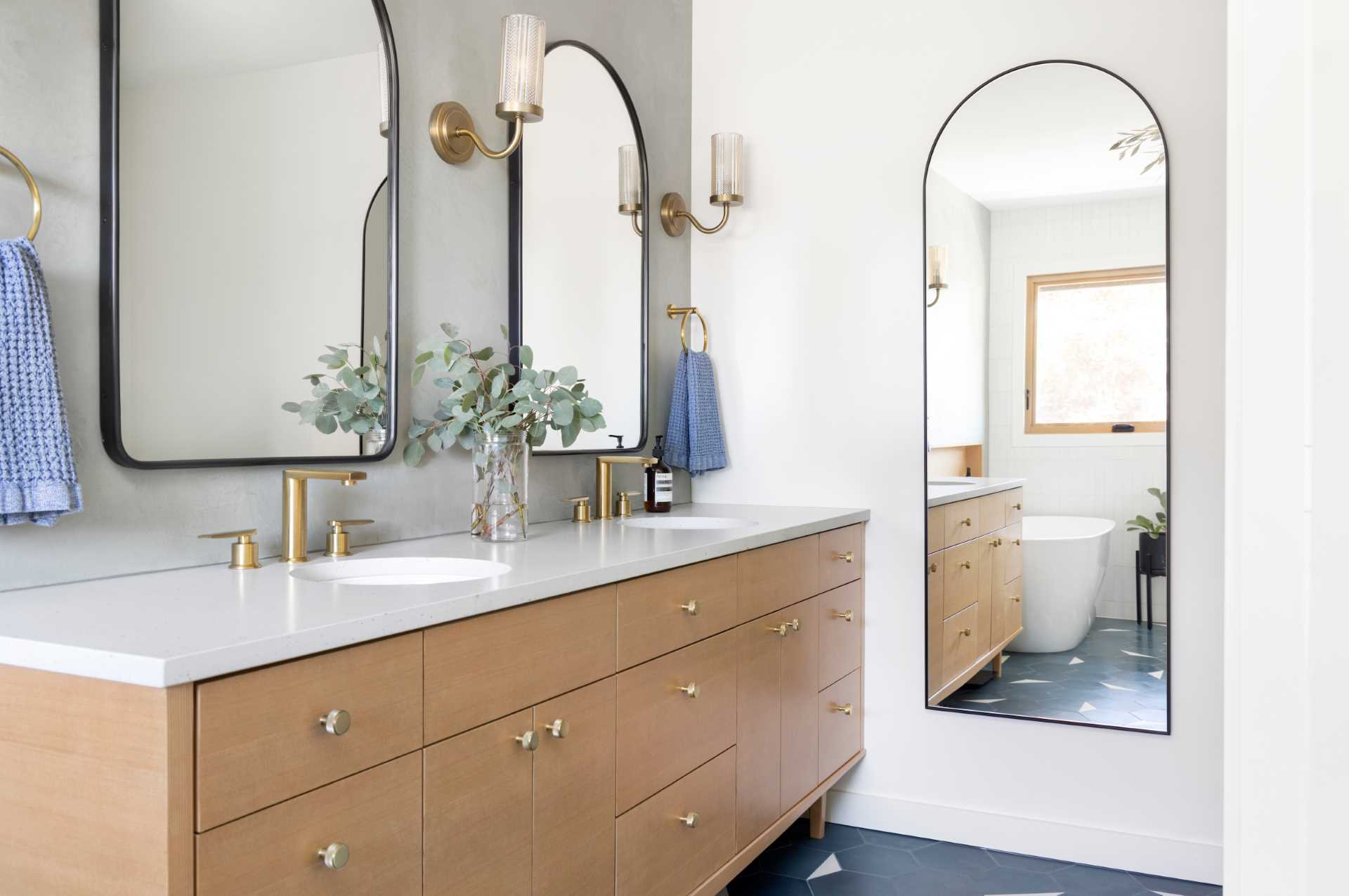This ensuite bathroom includes a mid-century modern inspired tile flooring, a walk-in shower with a bench, white tiled walls, a freestanding bathtub with wood shelving niche, and a wood vanity.