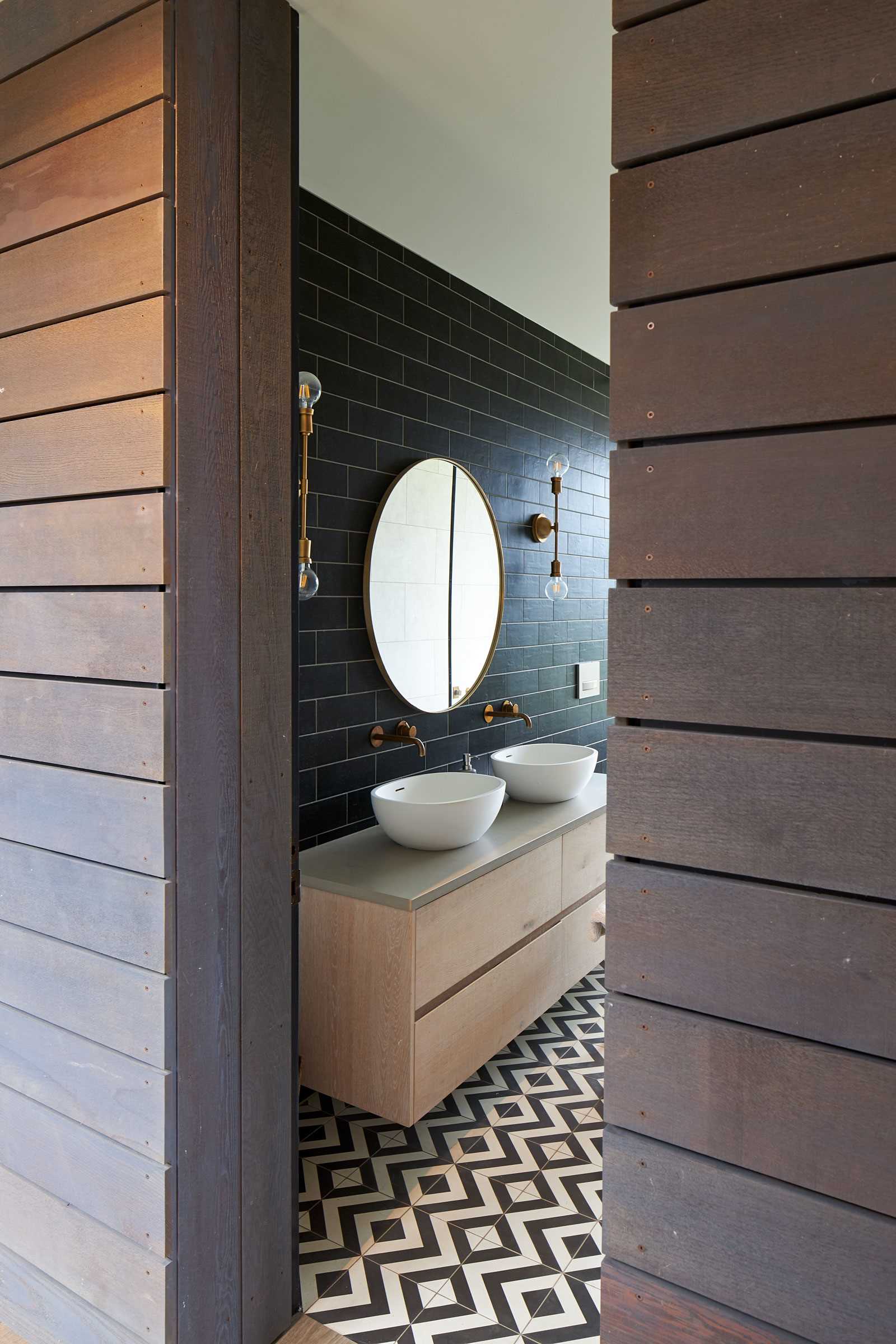 In this modern bathroom, black subway tiles line the wall, while graphic black and white tiles are featured on the floor. A floating wood vanity adds a natural element, and the freestanding bathtub is positioned in front of the floor-to-ceiling window.