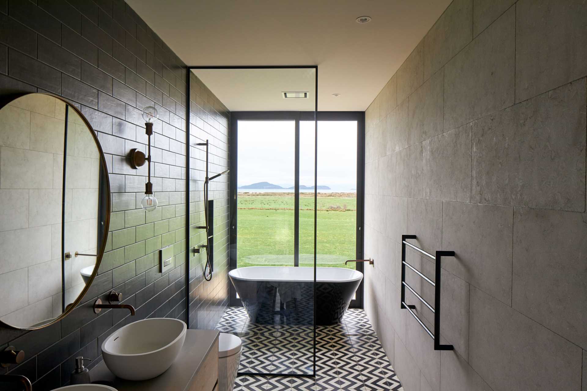 In this modern bathroom, black subway tiles line the wall, while graphic black and white tiles are featured on the floor. A floating wood vanity adds a natural element, and the freestanding bathtub is positioned in front of the floor-to-ceiling window.