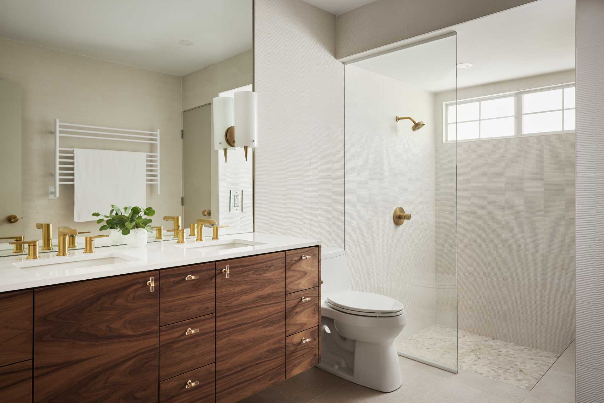 AFTER - This updated main bathroom has a sense of sophistication, with a double vanity with walnut cabinetry, metallic hardware, and a large mirror. In the shower, the glass block wall has been replaced with a solid wall, and the shower curtain has been replaced by a glass shower screen.