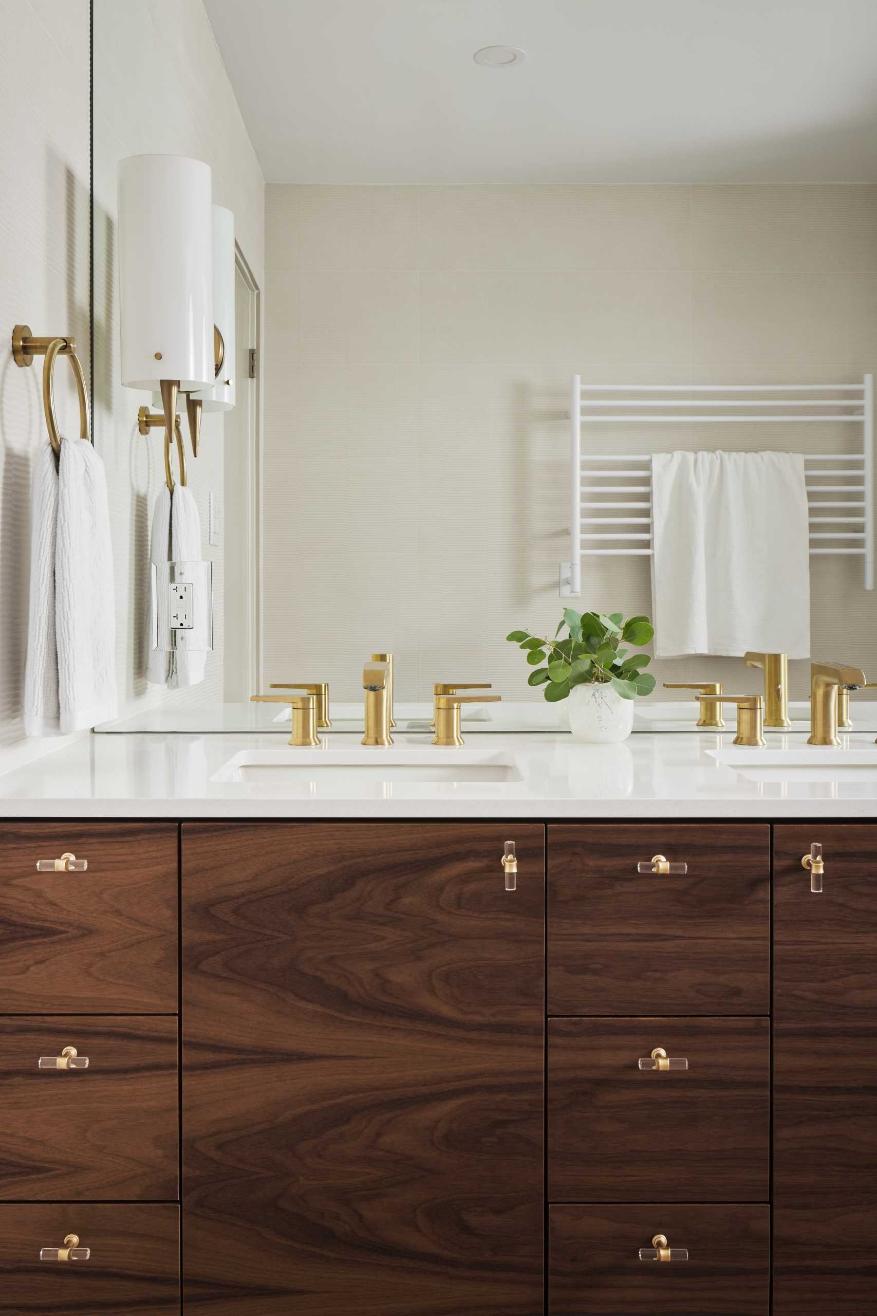 AFTER - This updated main bathroom has a sense of sophistication, with a double vanity with walnut cabinetry, metallic hardware, and a large mirror. In the shower, the glass block wall has been replaced with a solid wall, and the shower curtain has been replaced by a glass shower screen.