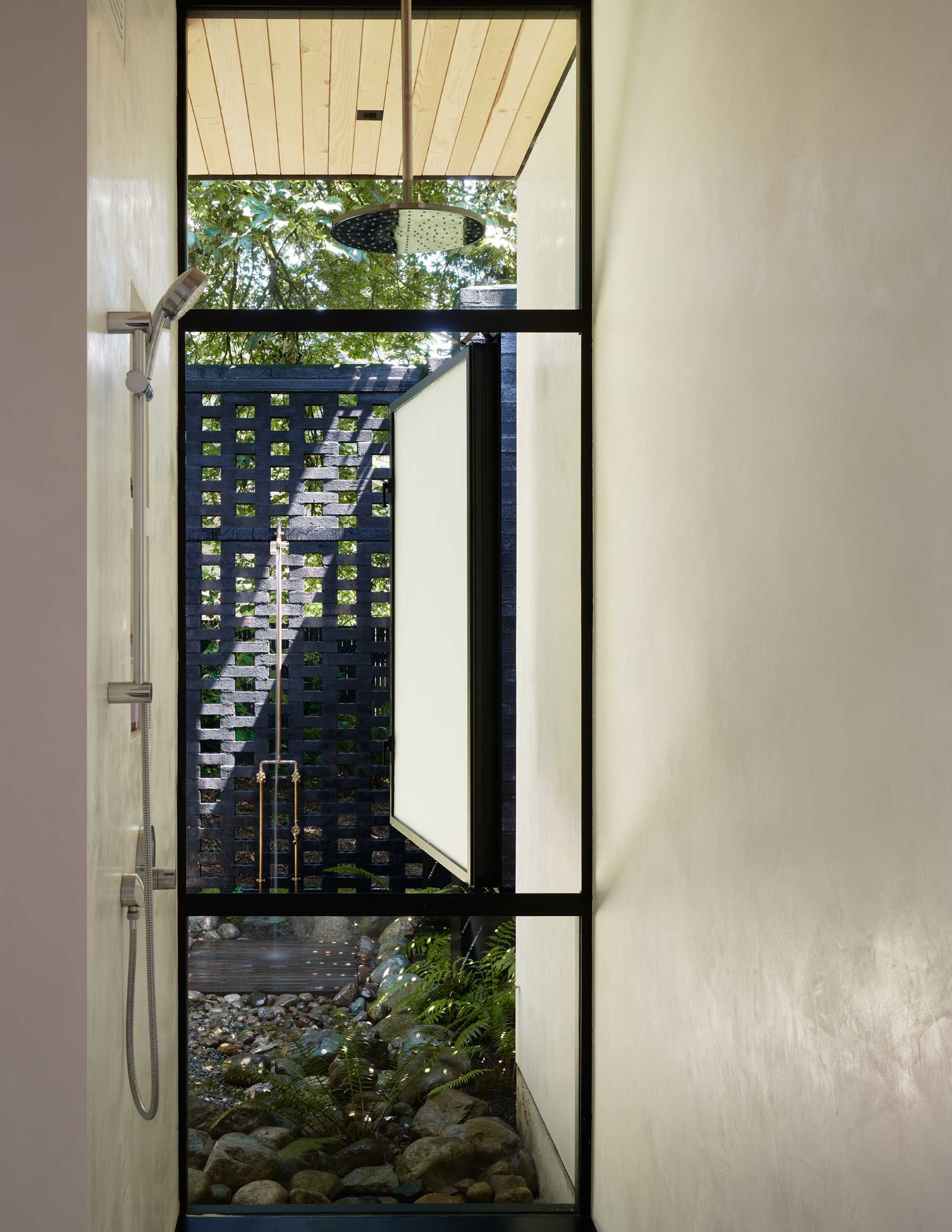 A modern home with an interior shower that has views of the outdoor shower.