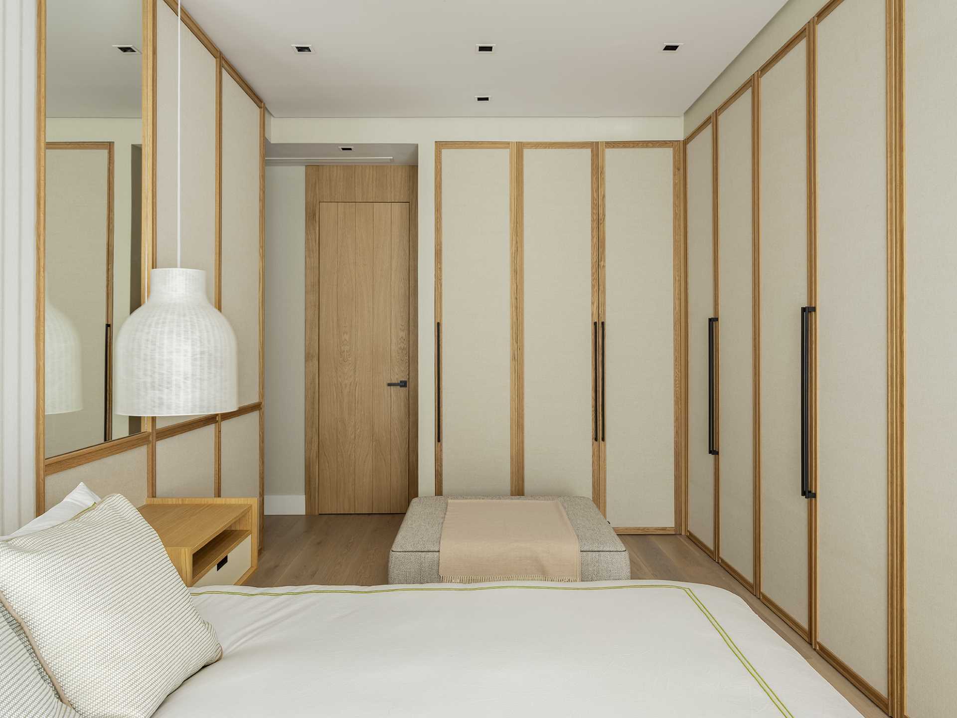 Textile panels and mirrors adorn the wall of this bedroom, while floating bedside tables have pendant lights that hang above them.