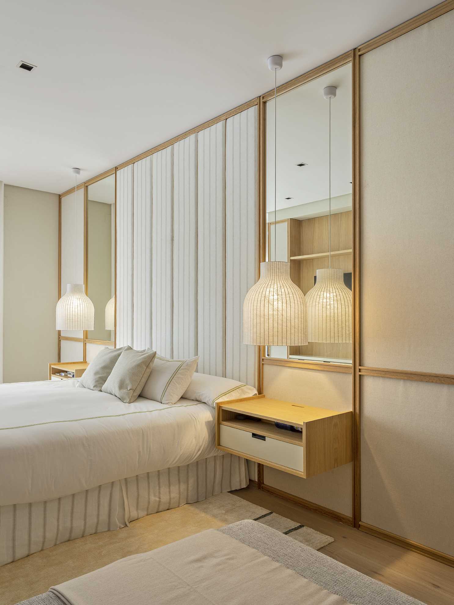 Textile panels and mirrors adorn the wall of this bedroom, while floating bedside tables have pendant lights that hang above them.