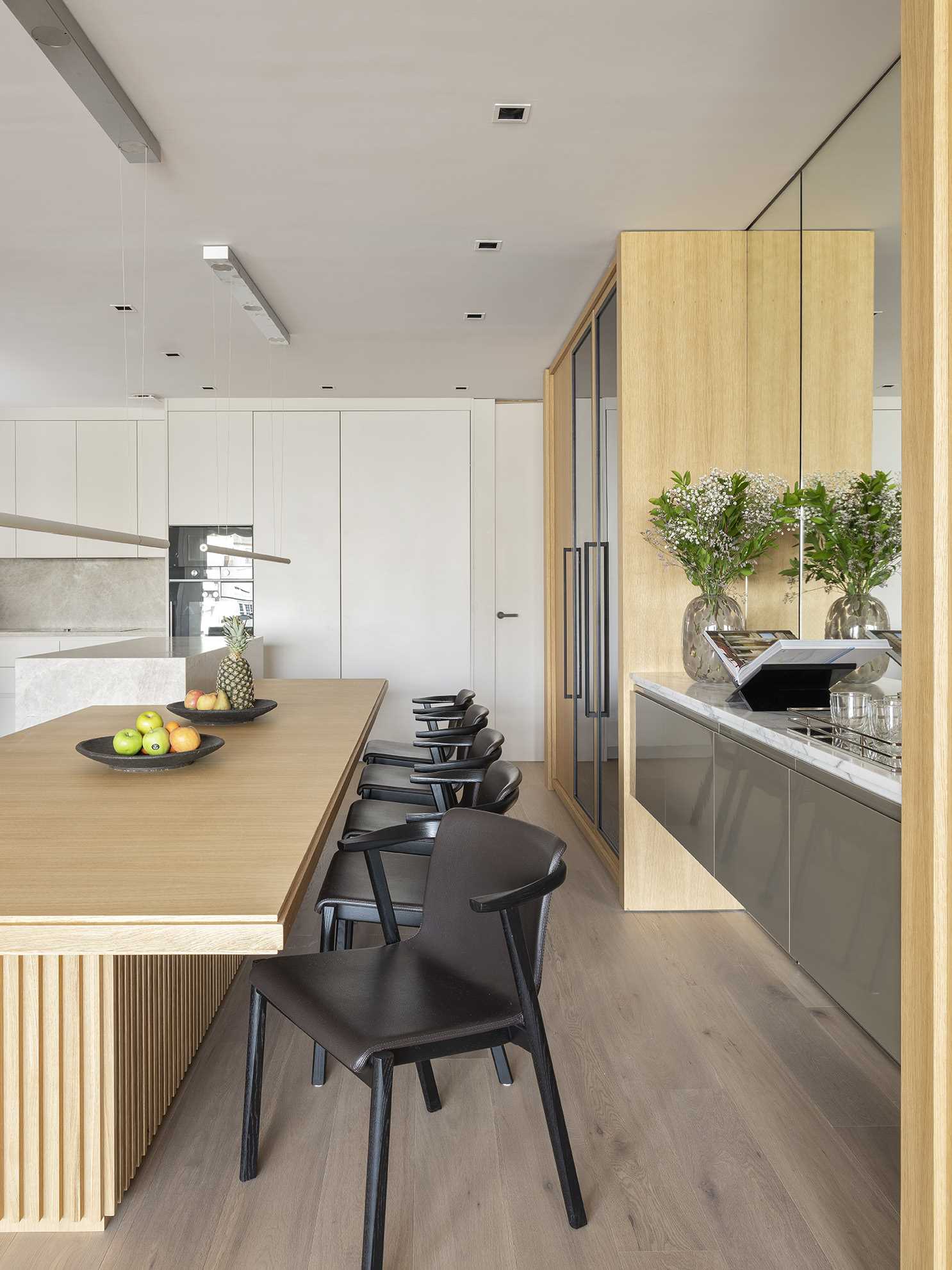 An open and spacious kitchen layout has been designed to invite engagement, where a marble bar and a long wooden dining table play host. A mirrored wall has also been included in this space.