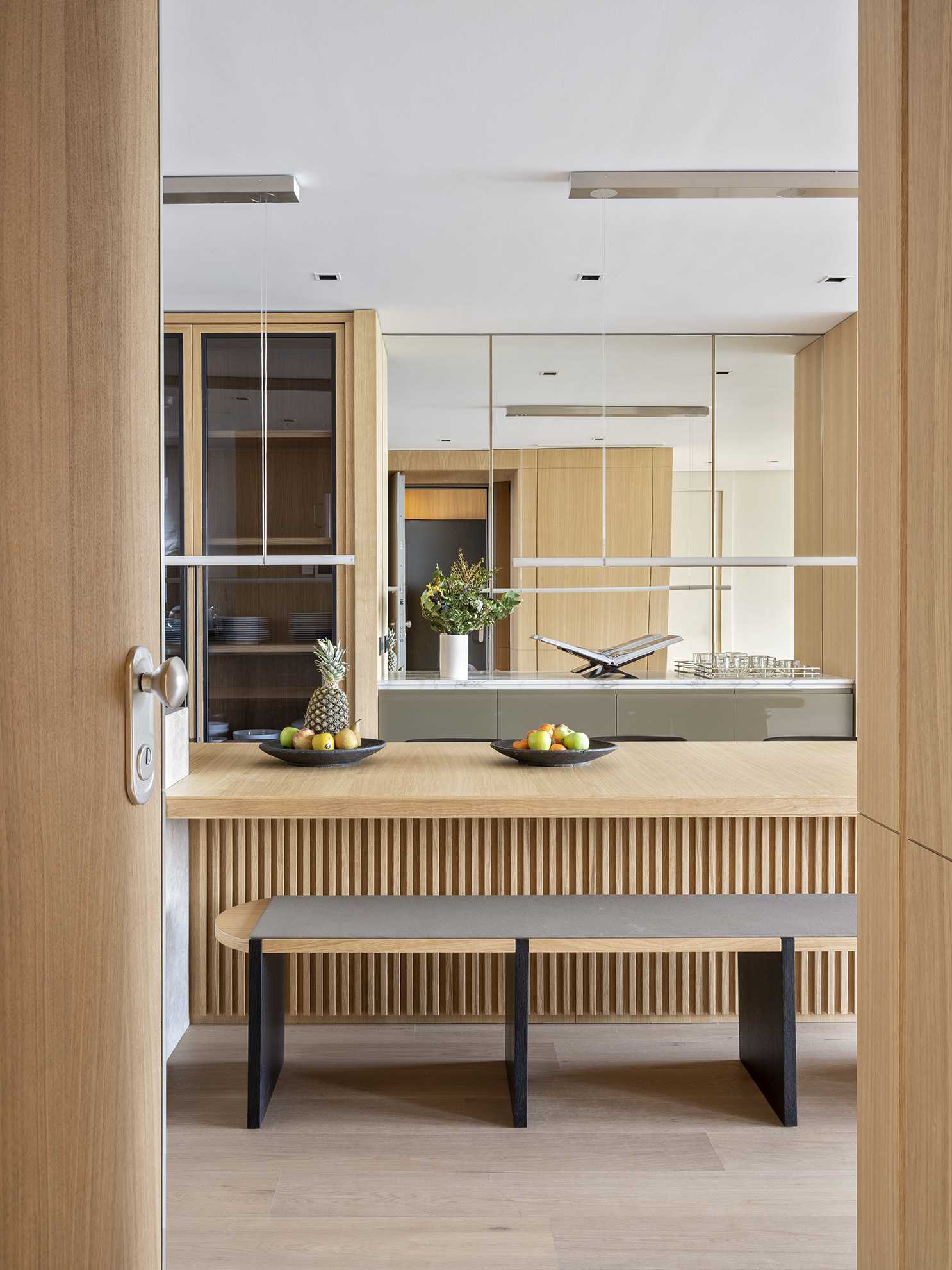 An open and spacious kitchen layout has been designed to invite engagement, where a marble bar and a long wooden dining table play host. A mirrored wall has also been included in this space.