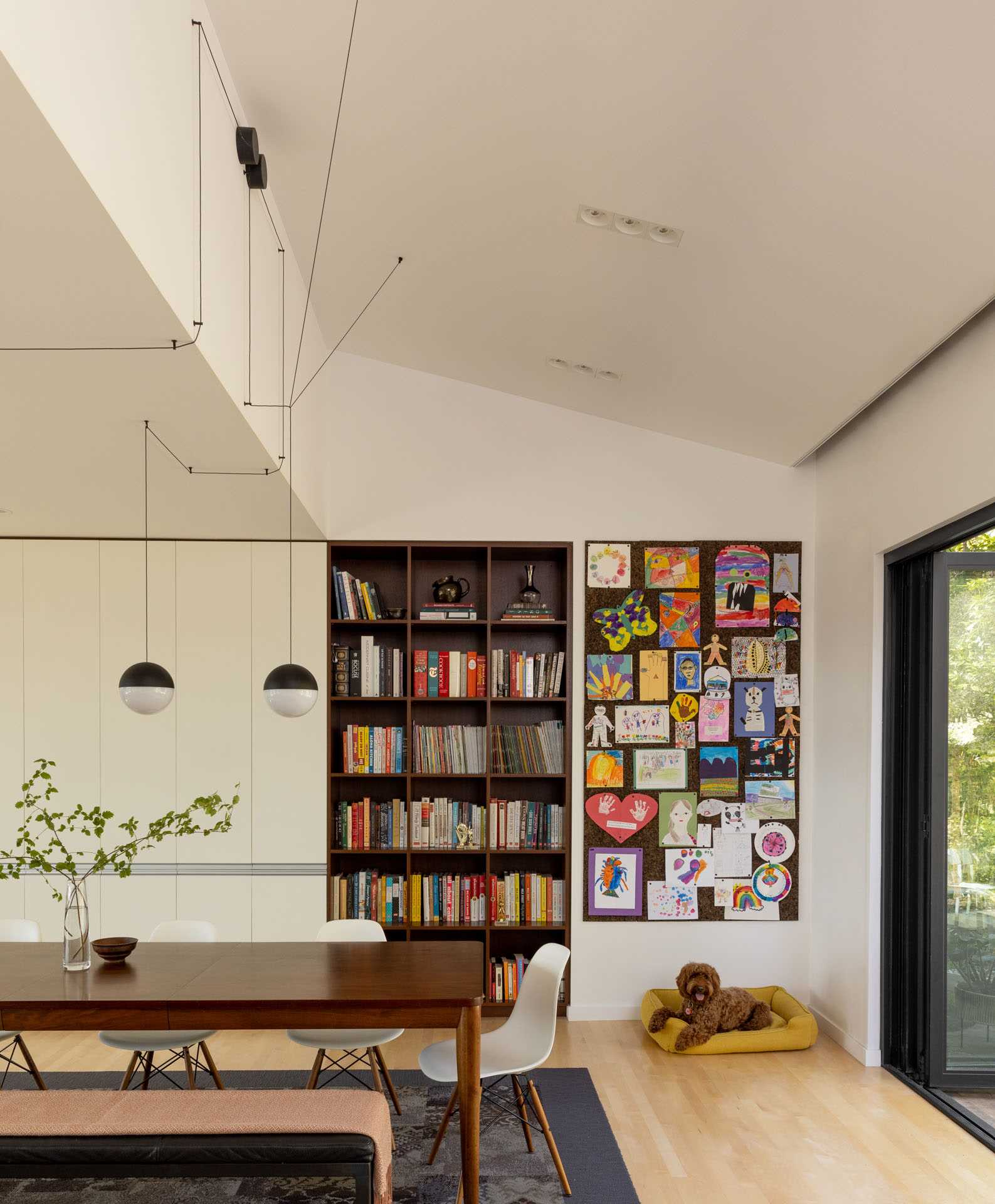 This modern dining room has a large wood dining table with bench and chair seating, as well as a wood bookshelf and art wall.