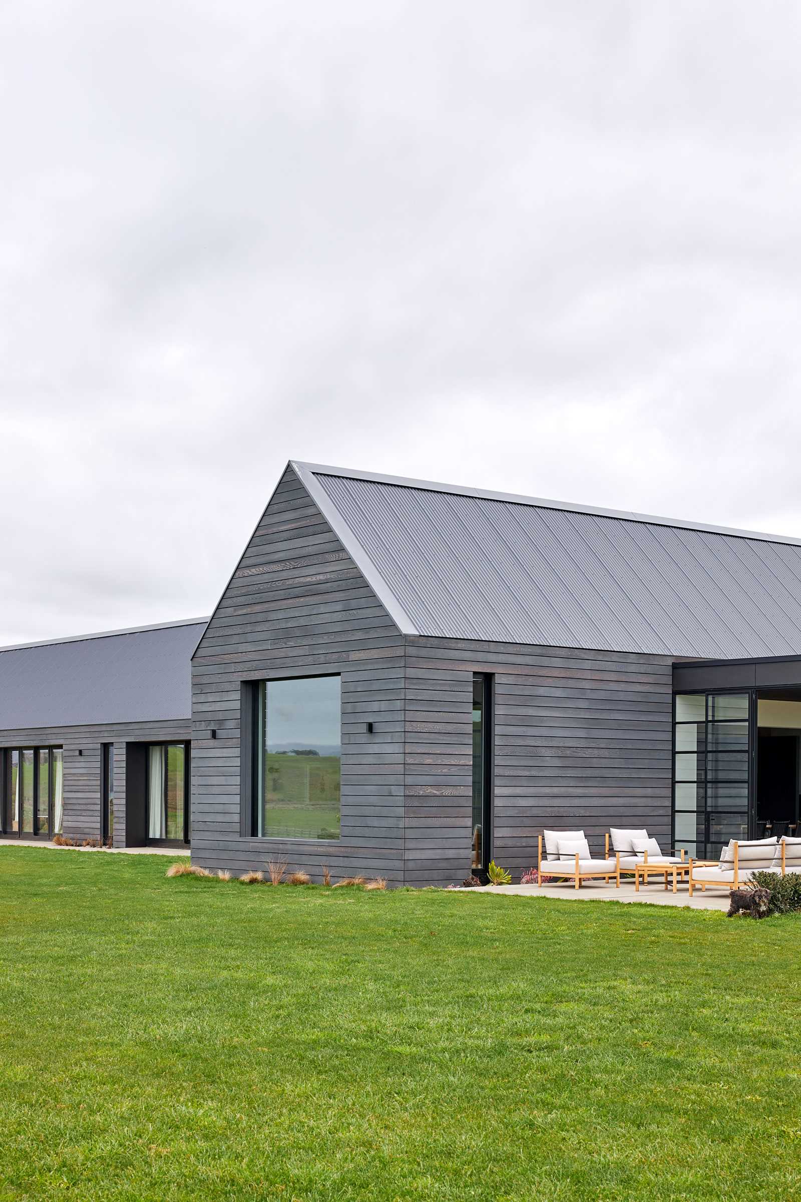 A contemporary farmhouse with grey-stained weathered wood siding and a standing seam grey metal roof.