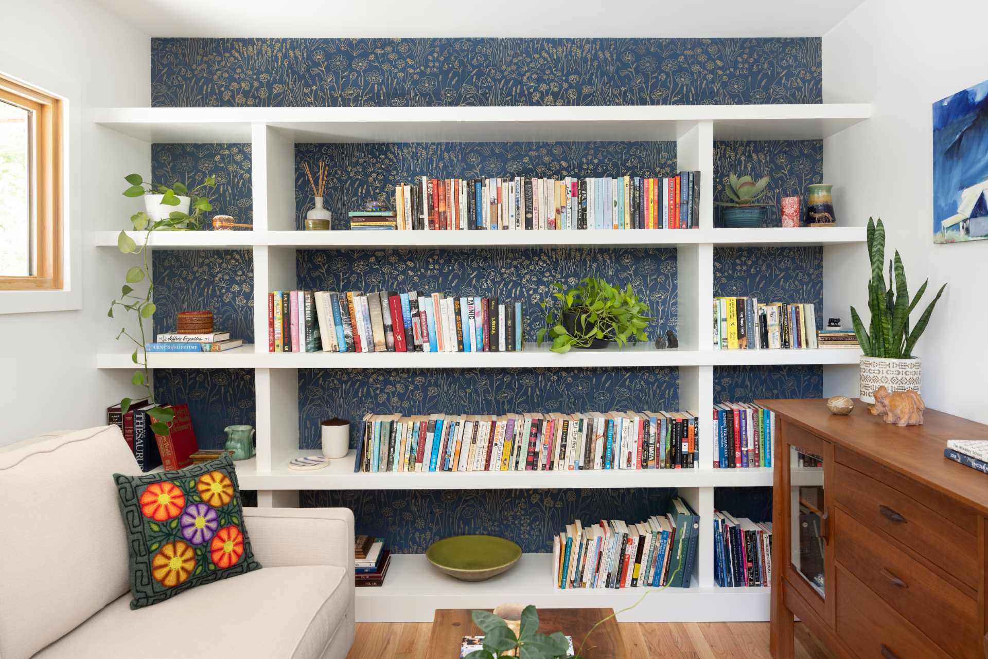 This modern home office includes a wallpapered wall with a delicate print that creates a backdrop for the white shelving that spans the wall.