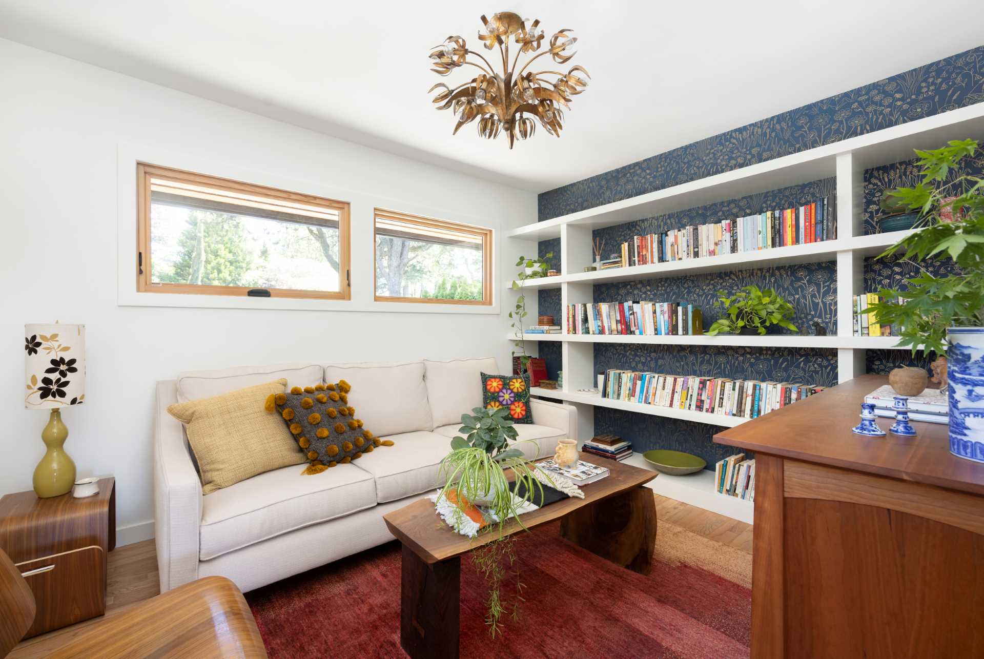 This modern home office includes a wallpapered wall with a delicate print that creates a backdrop for the white shelving that spans the wall.