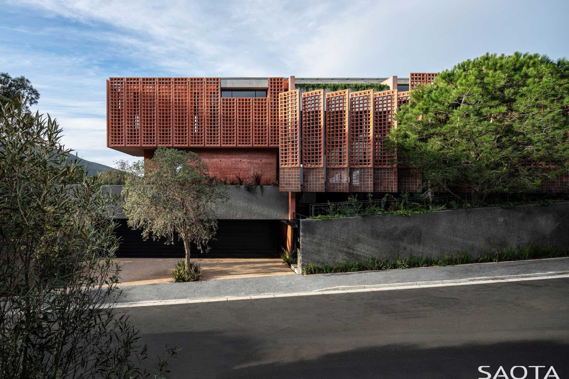 A modern home with distinctive red-pigmented concrete, which can be seen on the angled pre-cast concrete screens that are mounted on steel frames.