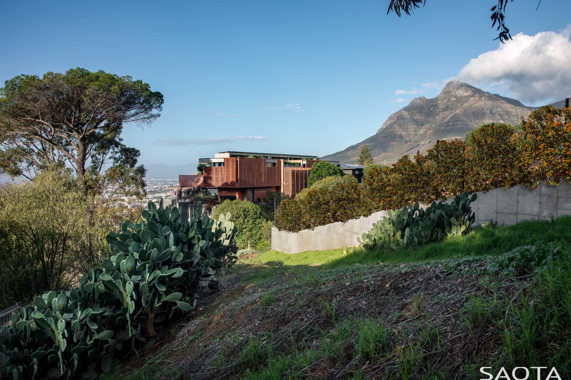 A modern home with distinctive red-pigmented concrete, which can be seen on the angled pre-cast concrete screens that are mounted on steel frames.