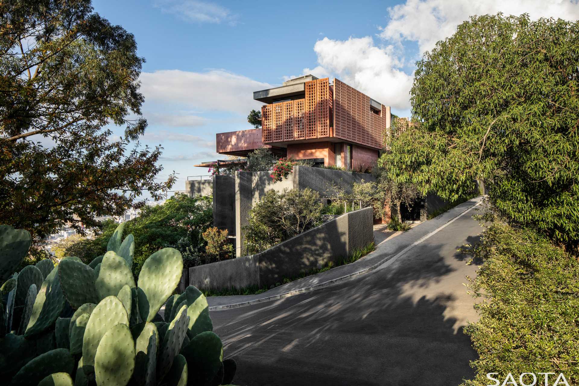 A modern home with distinctive red-pigmented concrete, which can be seen on the angled pre-cast concrete screens that are mounted on steel frames.