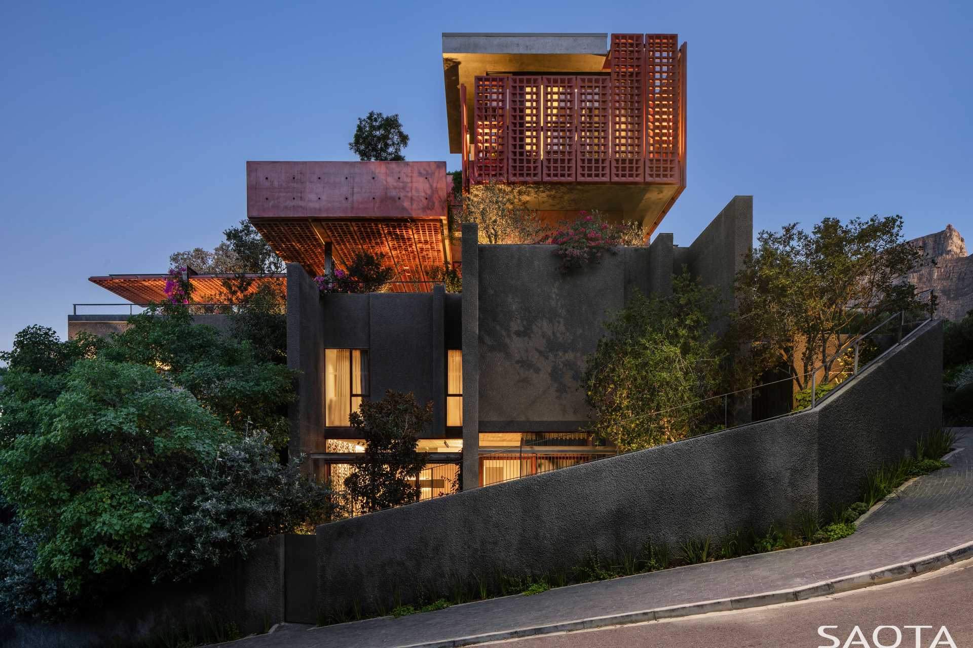 A modern home with distinctive red-pigmented concrete, which can be seen on the angled pre-cast concrete screens that are mounted on steel frames.