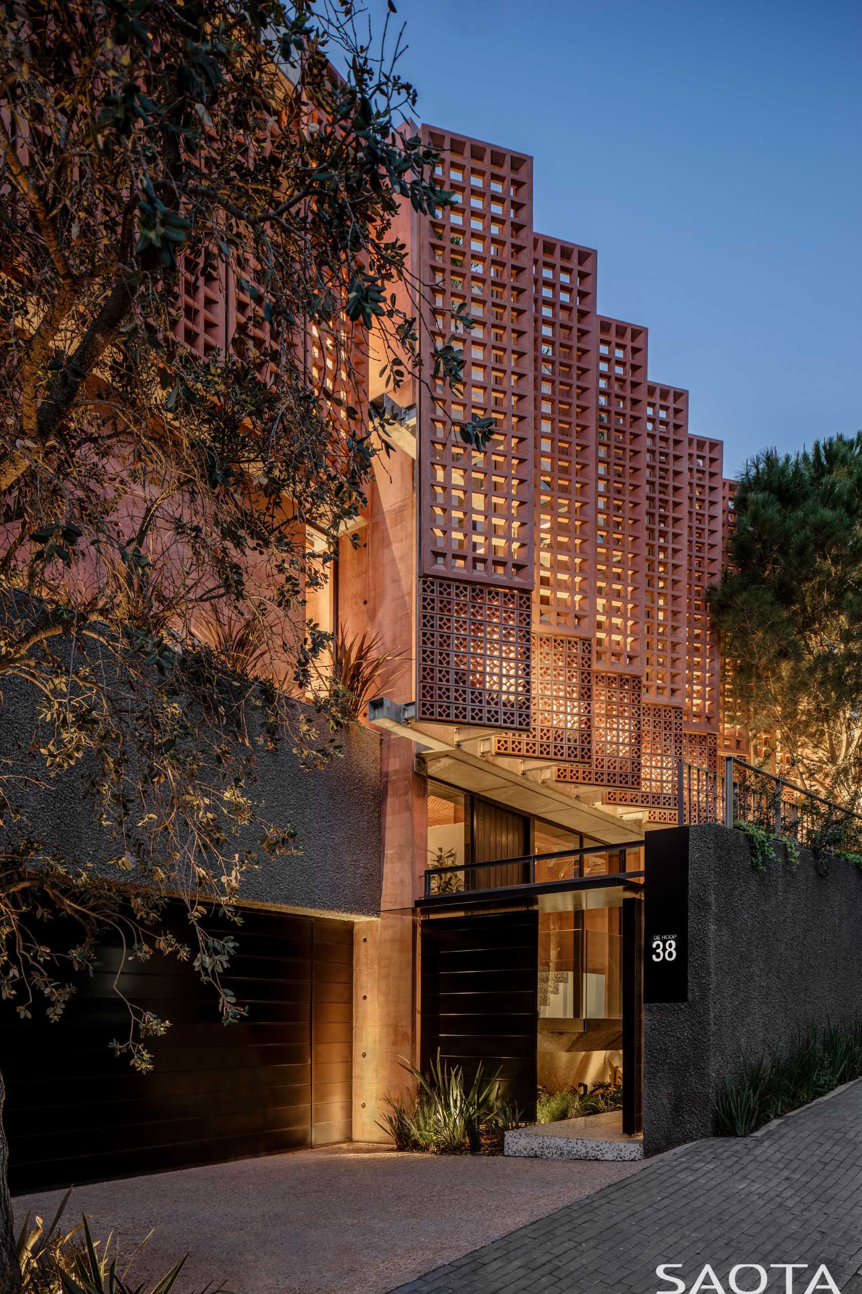 A modern home with distinctive red-pigmented concrete, which can be seen on the angled pre-cast concrete screens that are mounted on steel frames.