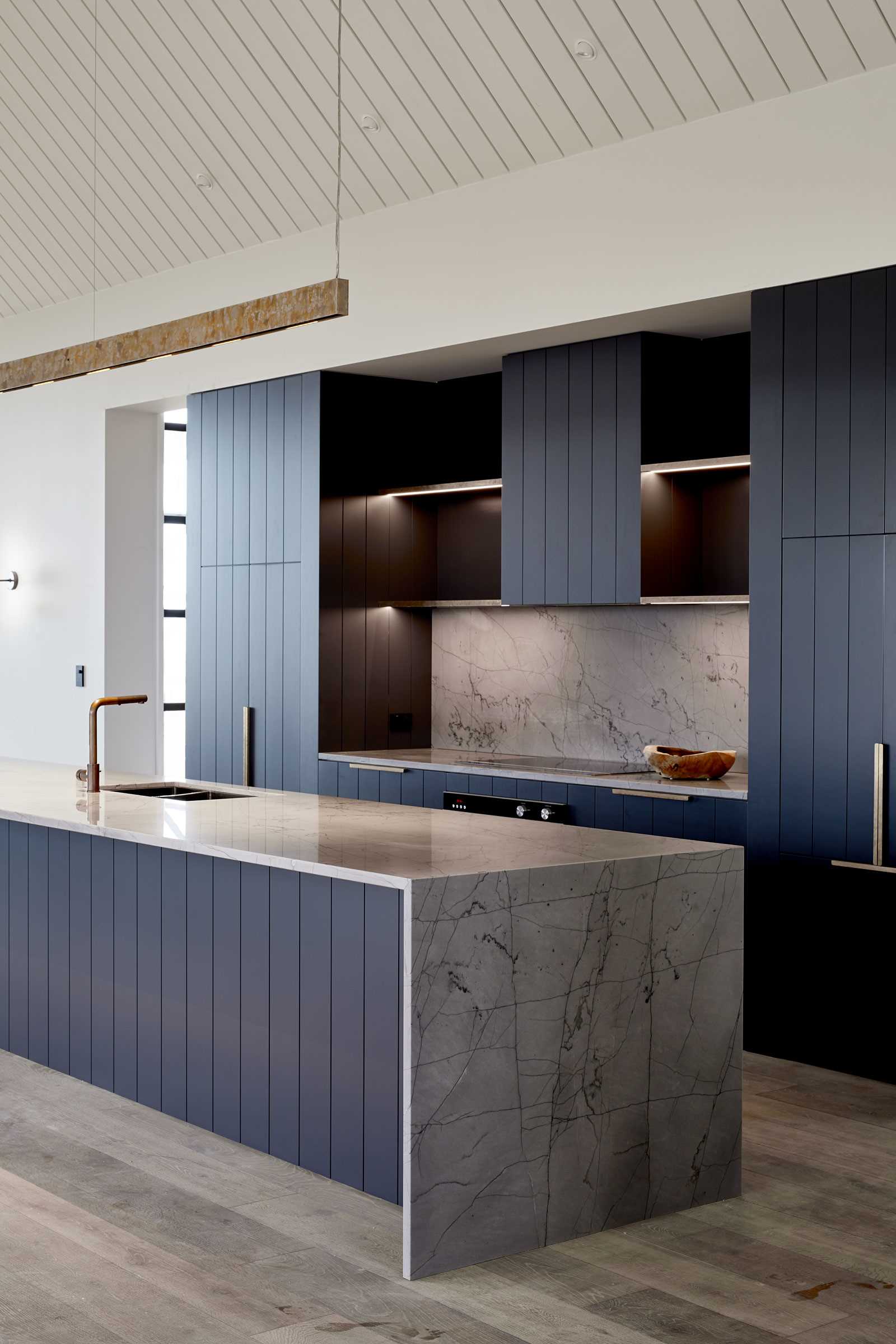 A modern kitchen has deep blue cabinetry with integrated appliances and a large island.