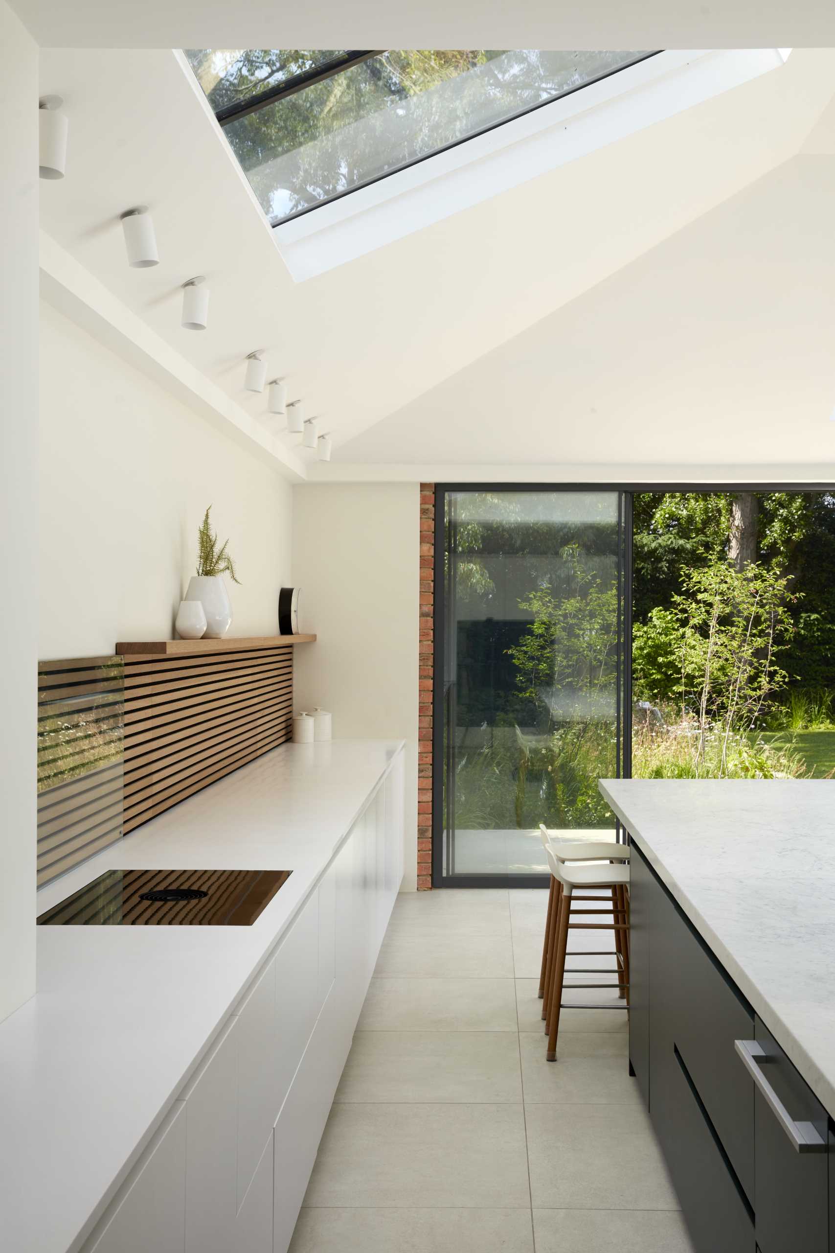 A modern kitchen with a large island, black and white cabinetry, and wood slat accent.