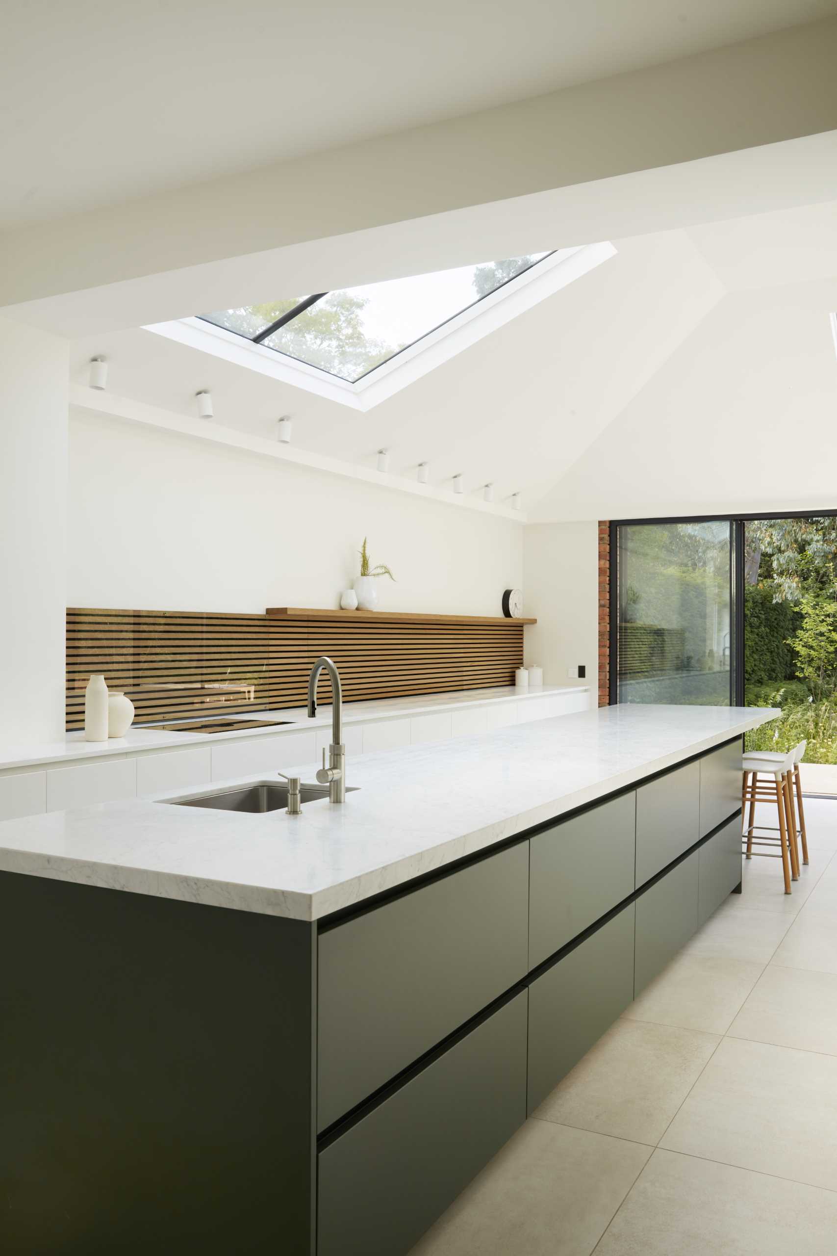 A modern kitchen with a large island, black and white cabinetry, and wood slat accent.