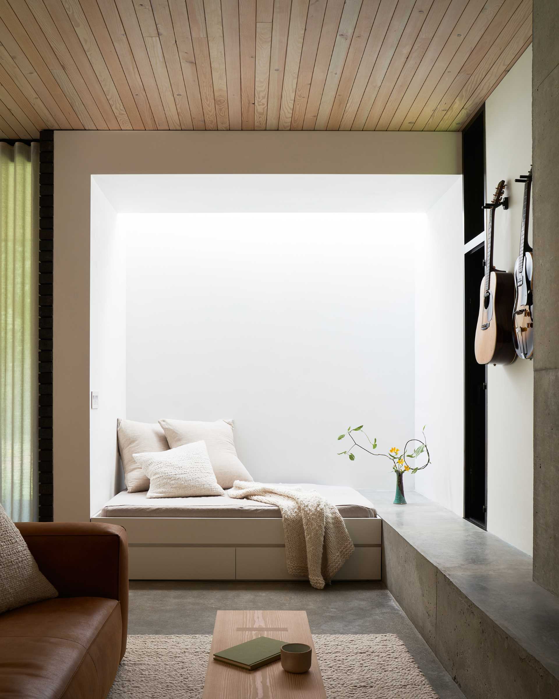 In this modern living room, the concrete hearth of the fireplace lines the wall and transitions into a bench with a skylight above.