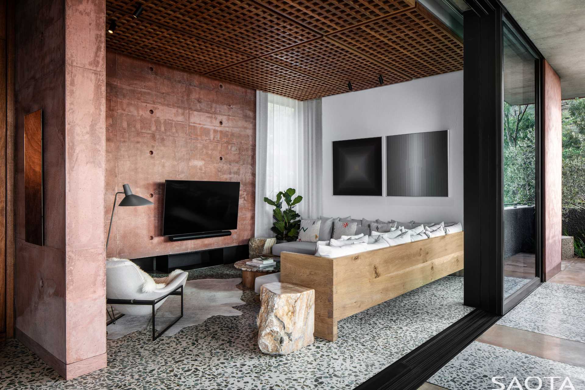 A TV room showcases red-pigmented concrete walls and an L-shaped couch.