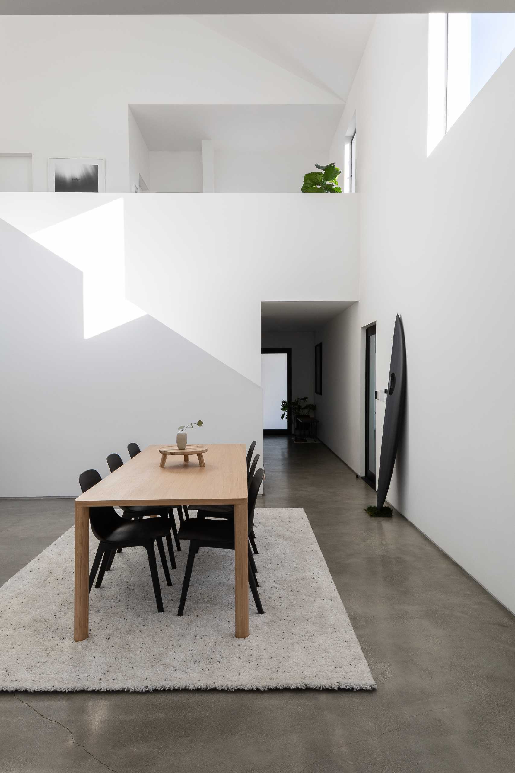 This modern double-height dining space is anchored by a rug in the open floor plan, and nearby the kitchen includes an island and black cabinets.