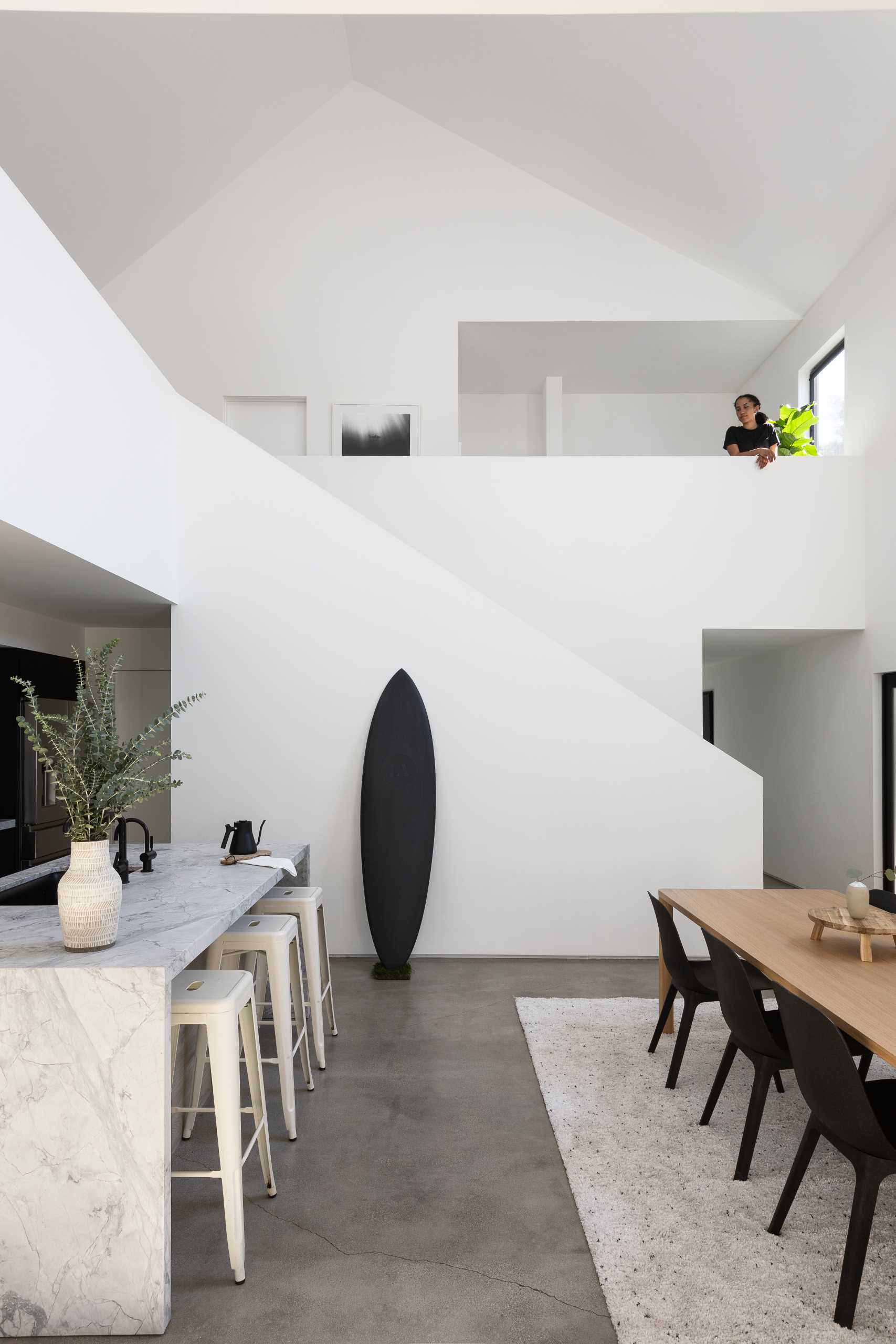 This modern double-height dining space is anchored by a rug in the open floor plan, and nearby the kitchen includes an island and black cabinets.