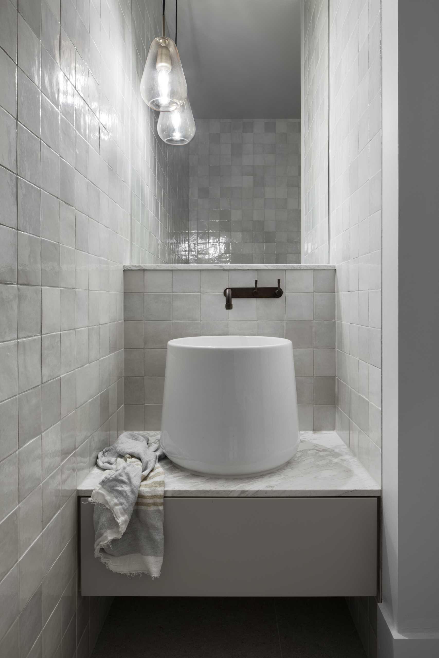 In this powder room, square tiles cover the walls, while the mirror makes the room feel larger than it is.