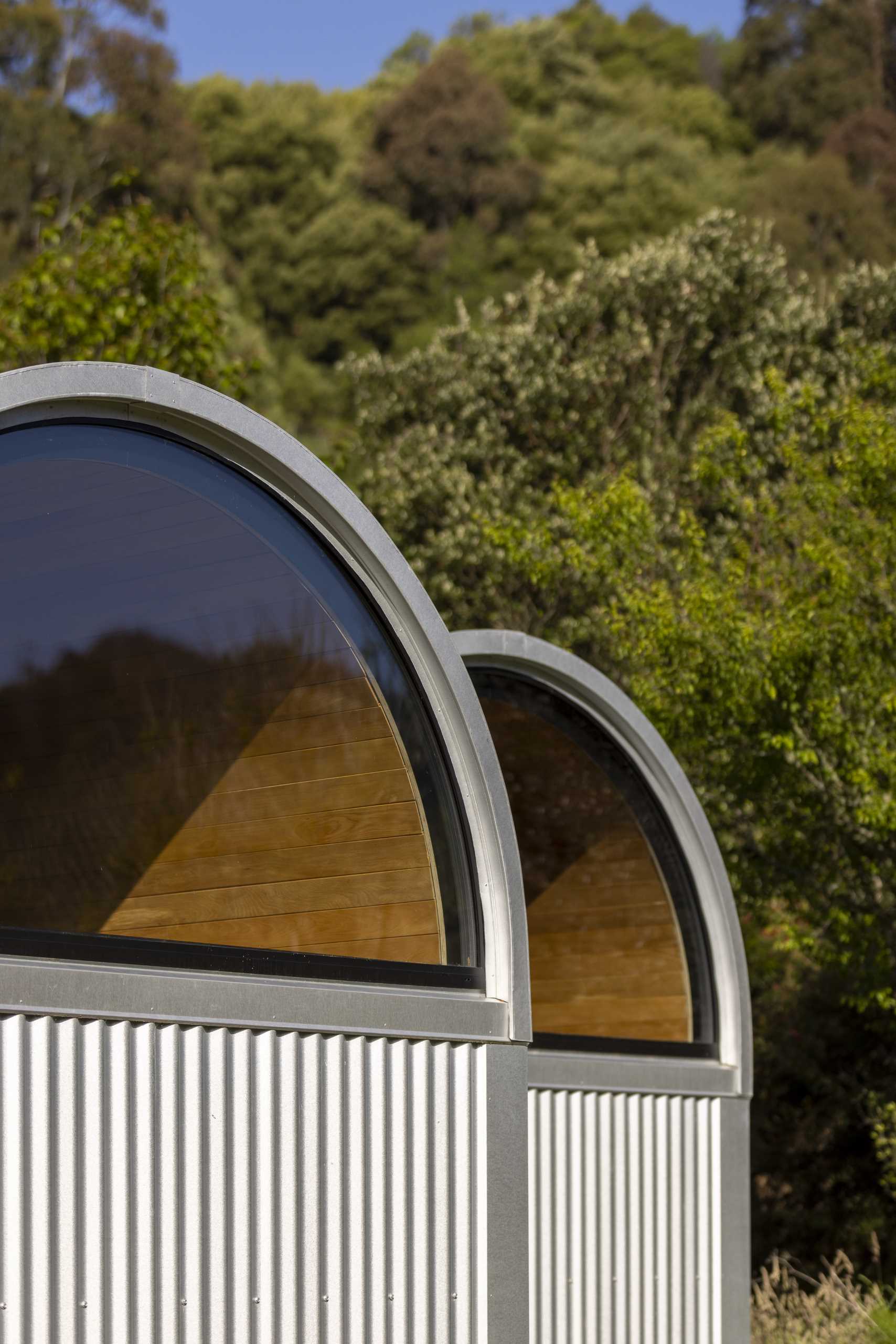 A modern and small one-bedroom home with a study, kitchen, loft, arched windows, and curved roof.