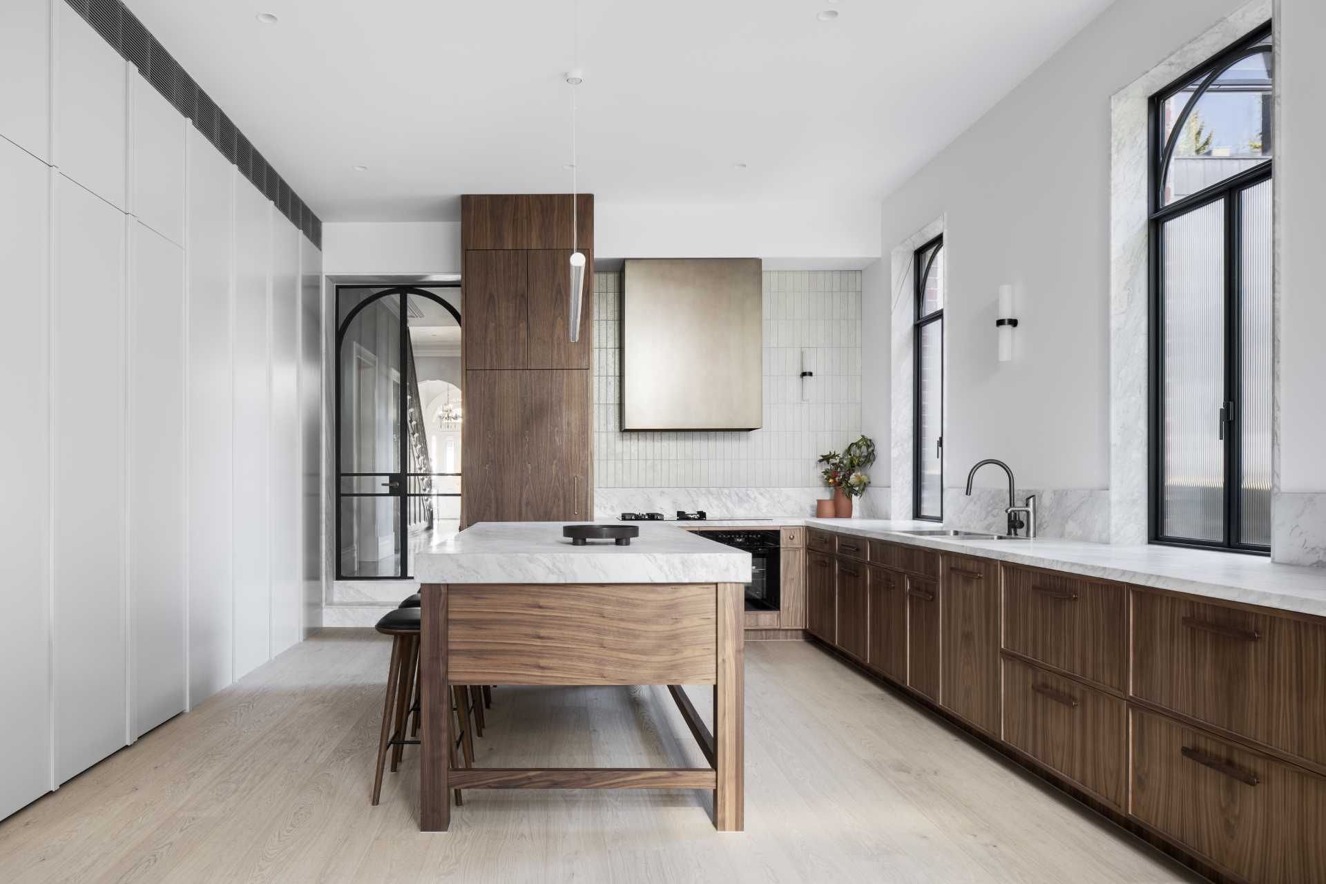 A modern kitchen with natural walnut veneer joinery and black steel-framed windows and doors.