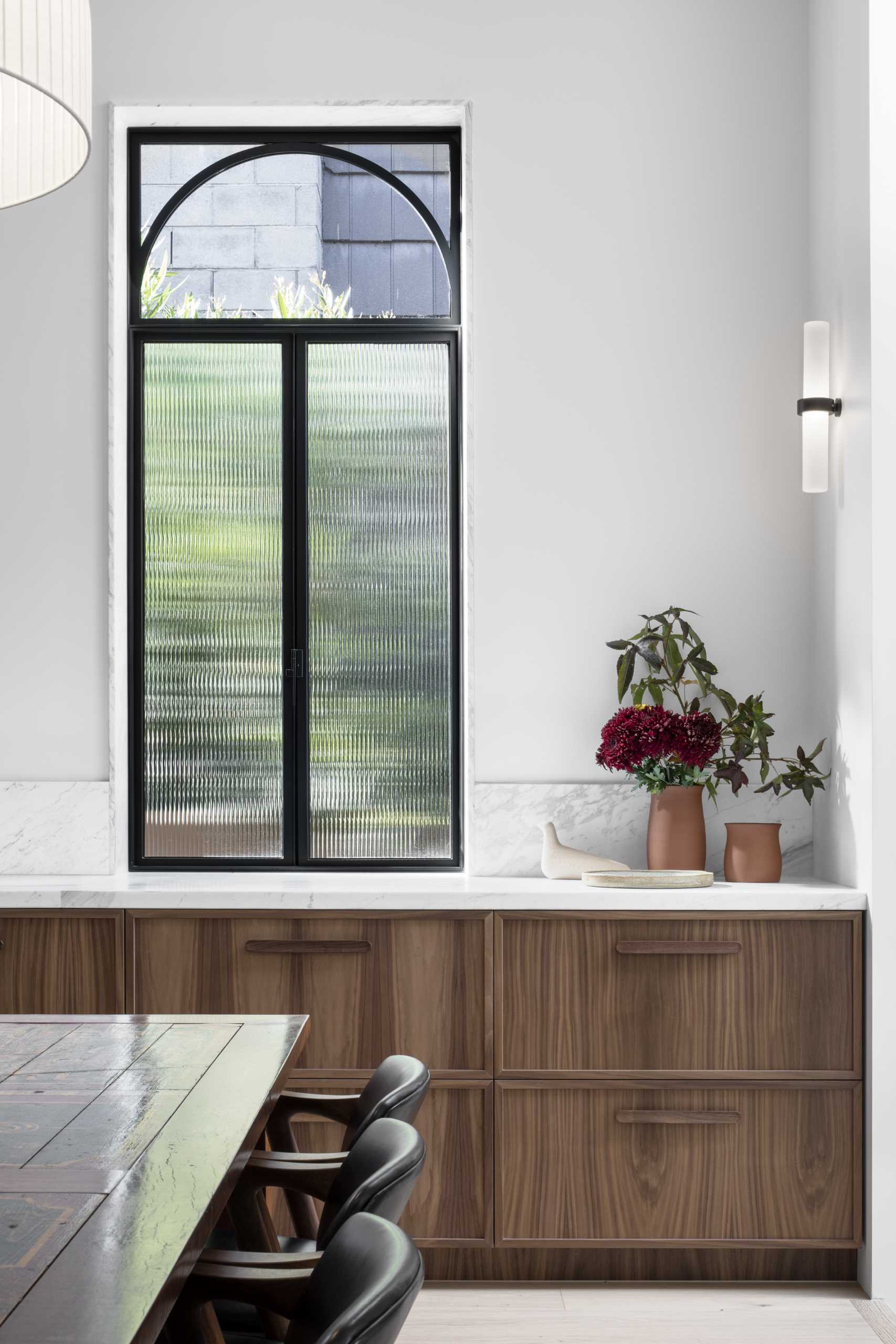 A modern kitchen with natural walnut veneer joinery and black steel-framed windows and doors.