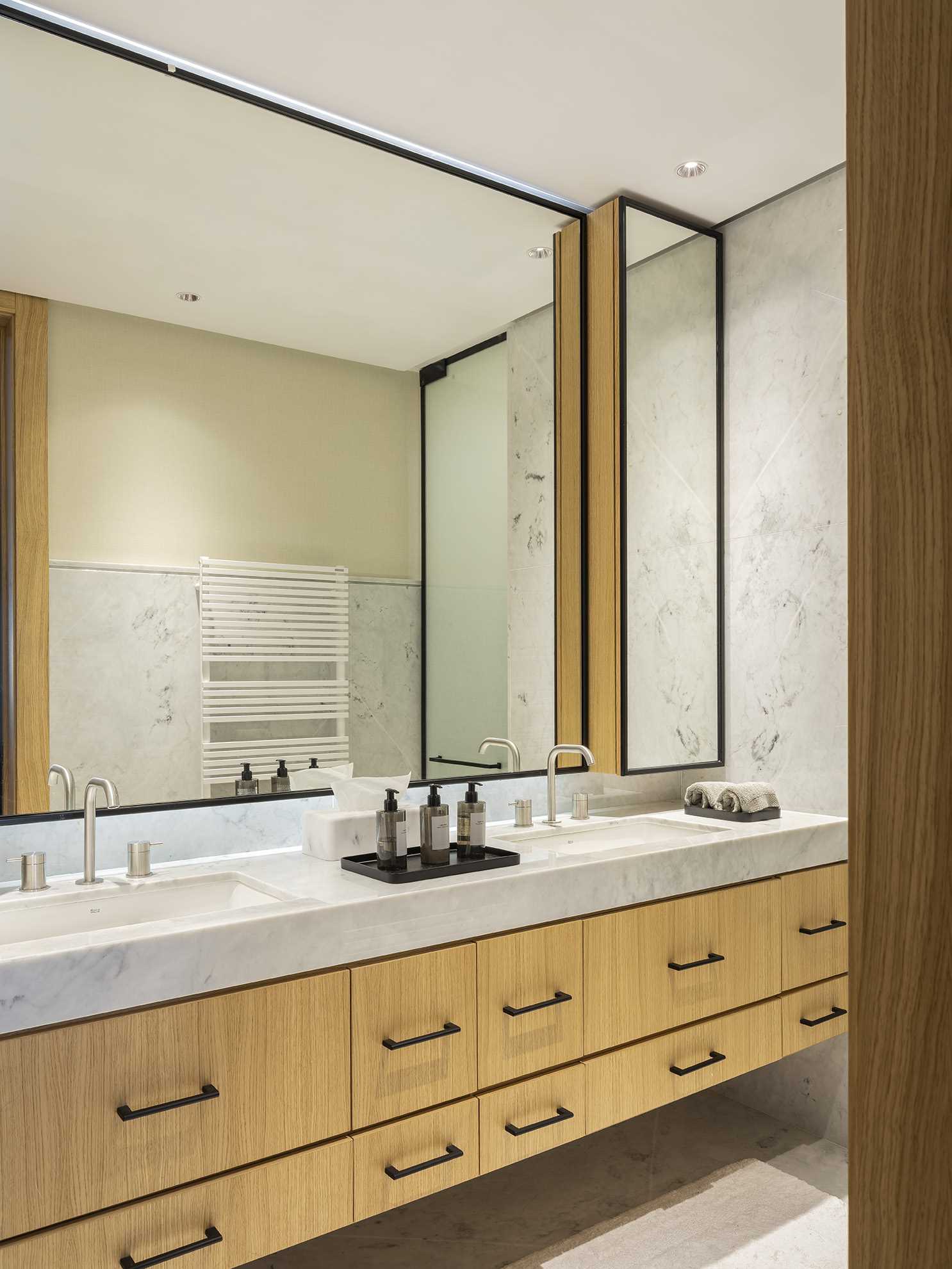 In this modern bathroom, a large double-sink wood vanity includes black accents that complement the black frames of the mirrors.