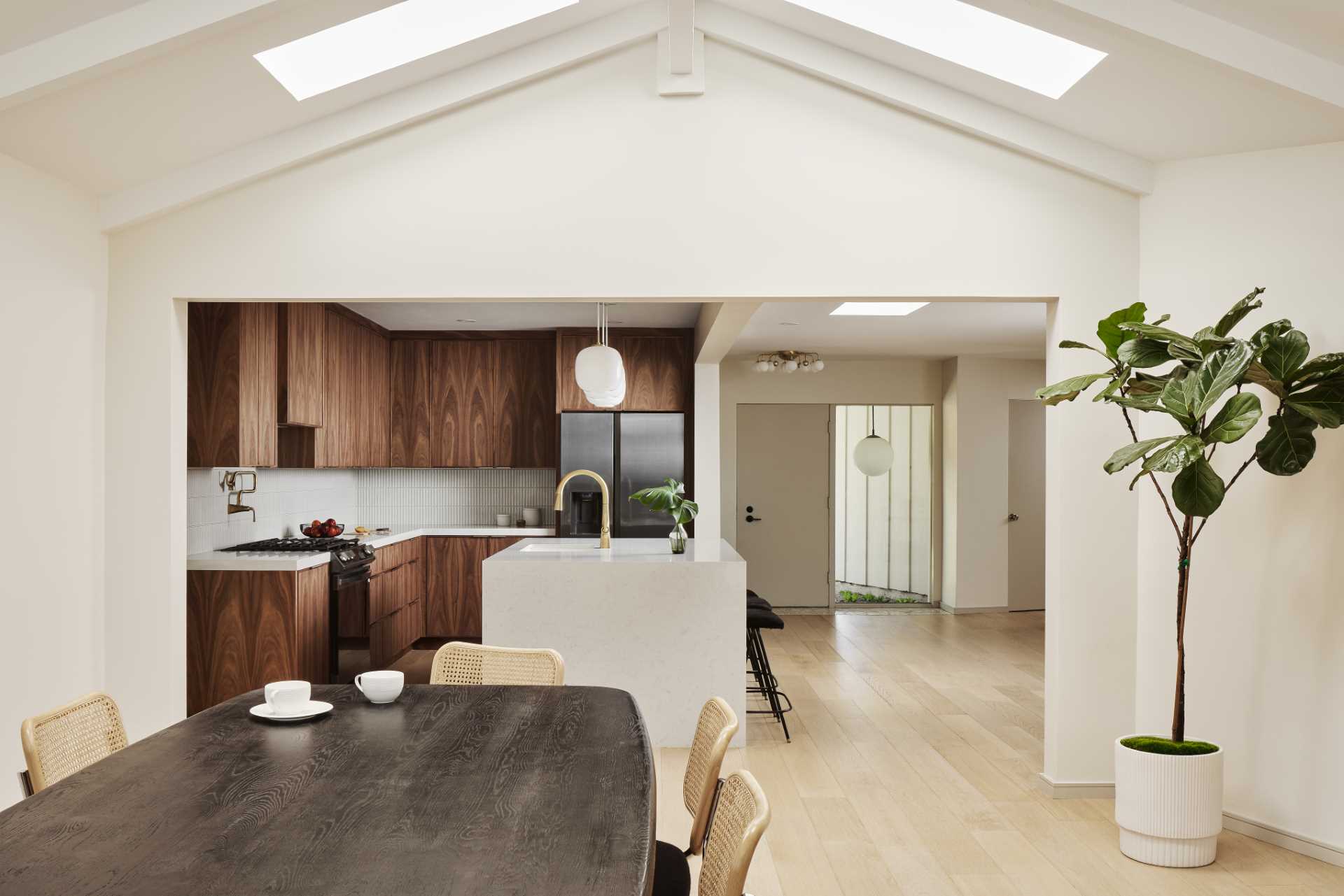 AFTER - This remodeled kitchen has been opened up to connect with the living room and dining room. New wood floors are featured throughout, and the warm custom walnut wood cabinets in the kitchen are paired with a thin vertical tile backsplash that wraps around the walls, while the countertop complements the large island.