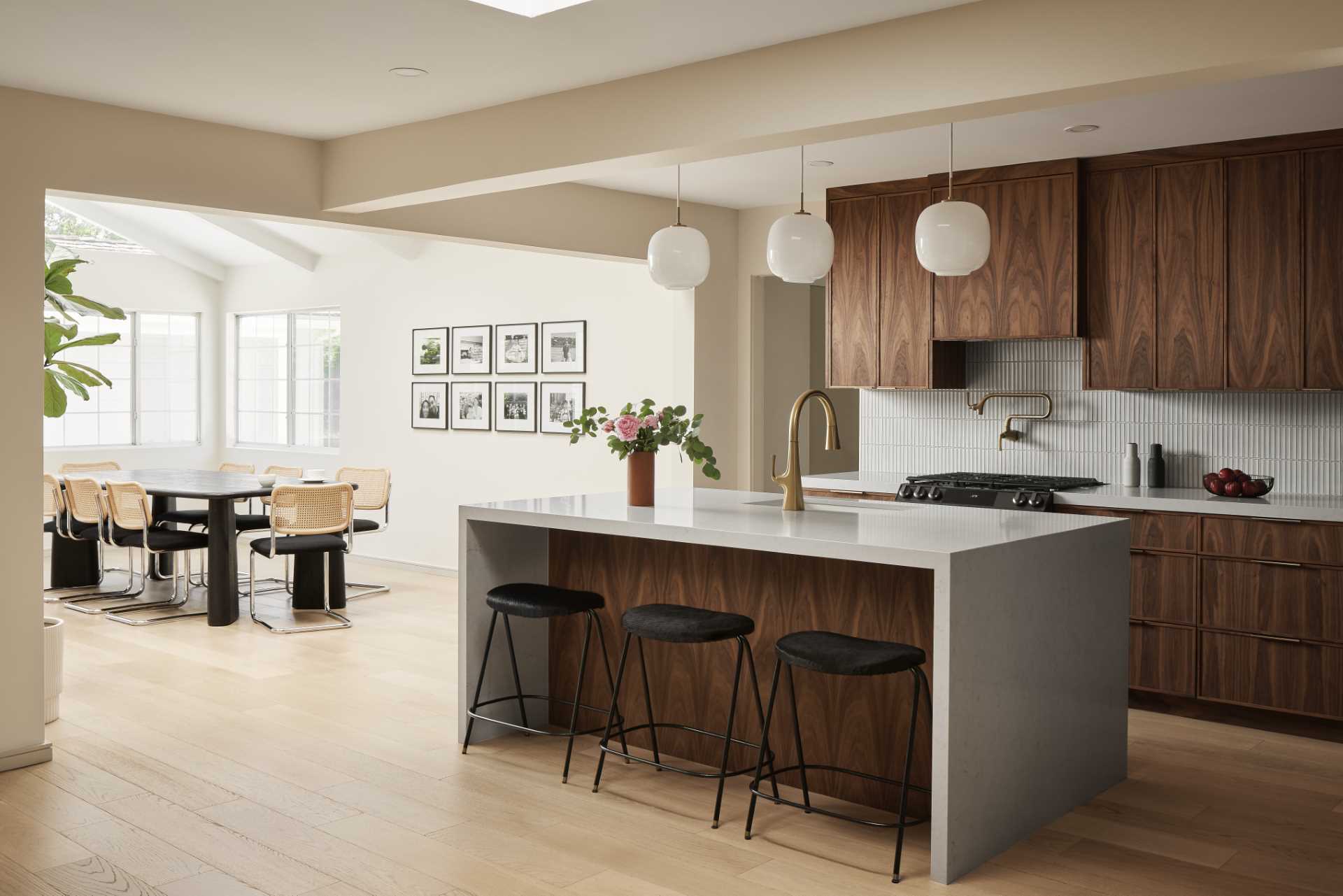 AFTER - This remodeled kitchen has been opened up to connect with the living room and dining room. New wood floors are featured throughout, and the warm custom walnut wood cabinets in the kitchen are paired with a thin vertical tile backsplash that wraps around the walls, while the countertop complements the large island.