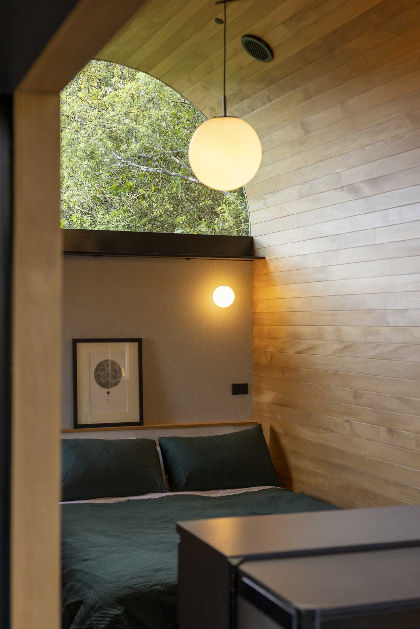 A modern bedroom with arched window and curved ceiling in a small one-bedroom home.