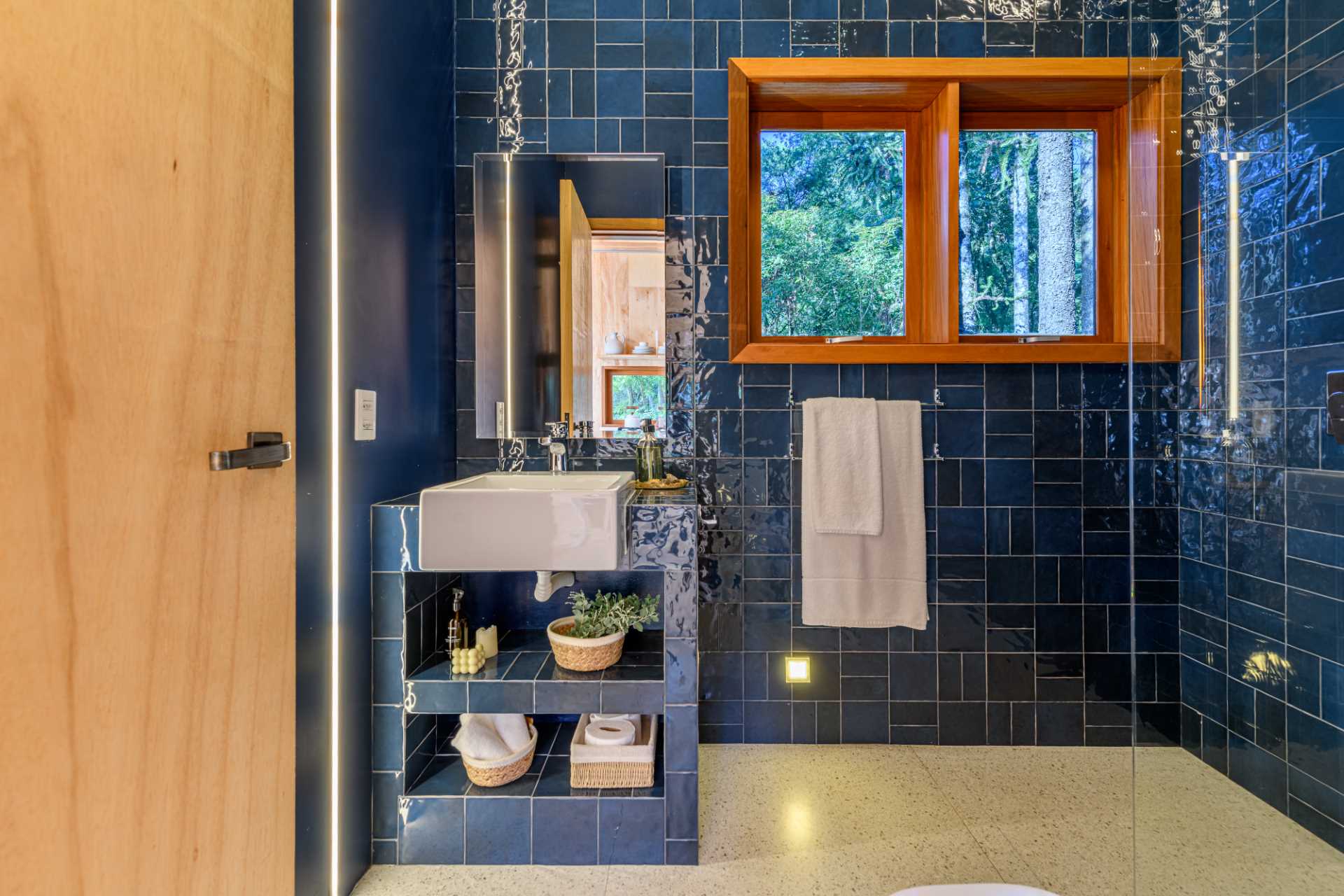 A modern bathroom in a tree house has walls and a vanity covered in blue tiles.