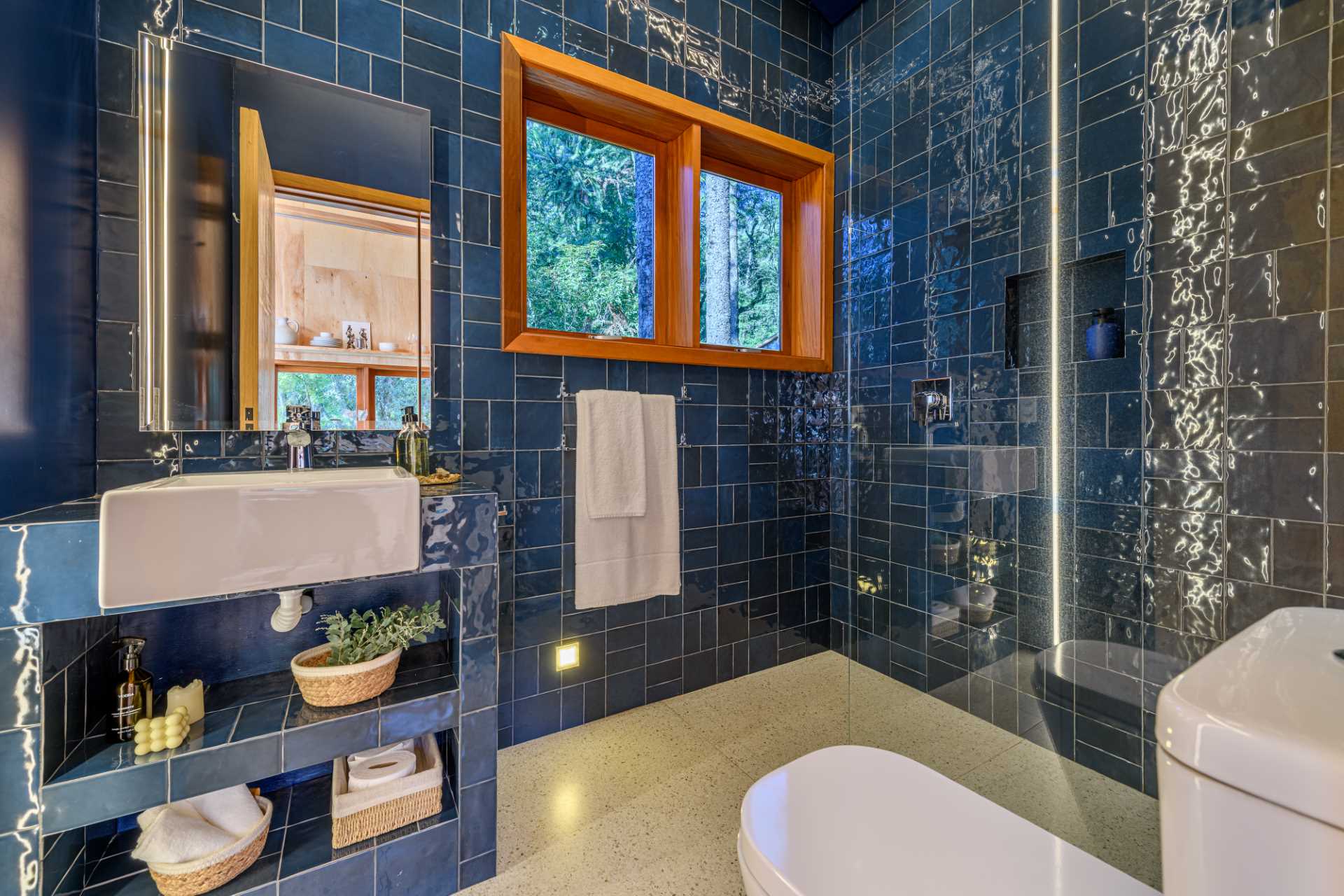 A modern bathroom in a tree house has walls and a vanity covered in blue tiles.