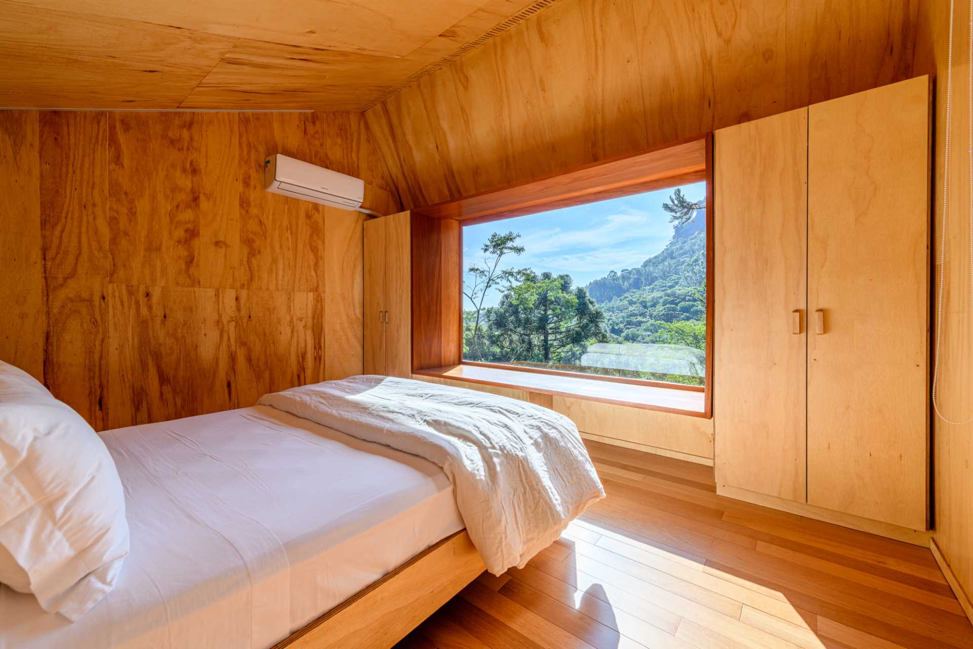 The bedroom of a modern tree house includes two closets, a large picture window, and a window bench.