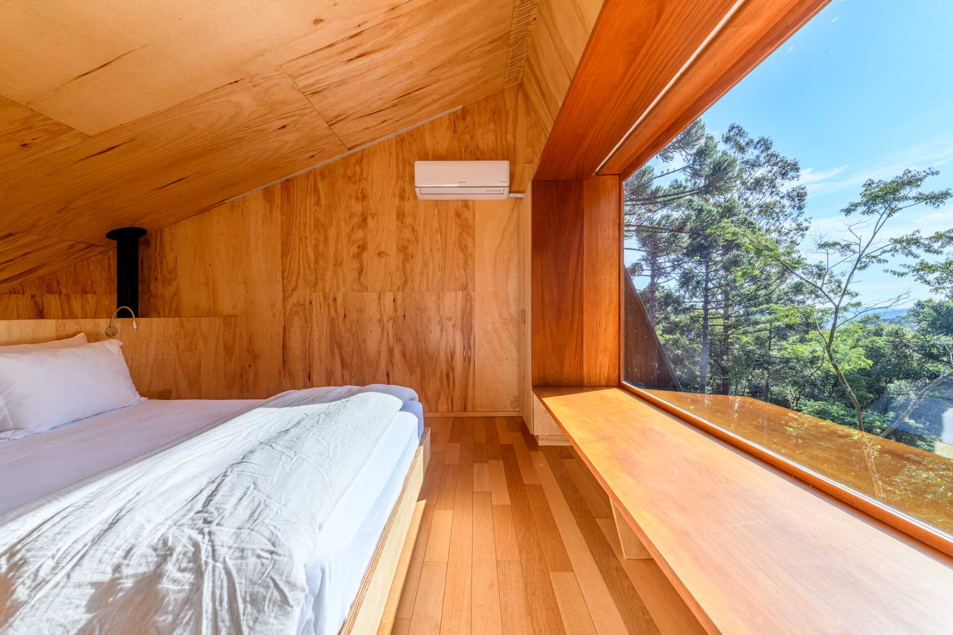 The bedroom of a modern tree house includes two closets, a large picture window, and a window bench.
