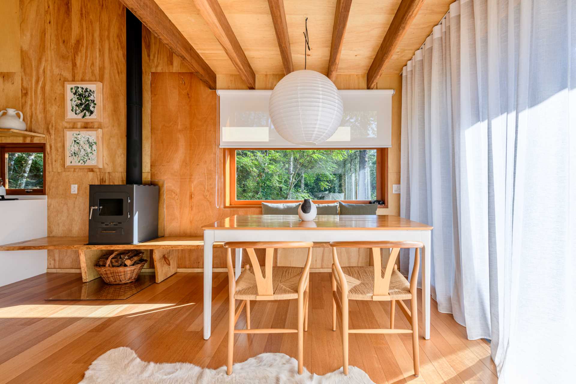 A modern tree house includes a dining area with a table and chairs, and a bench that runs underneath the window to the fireplace.