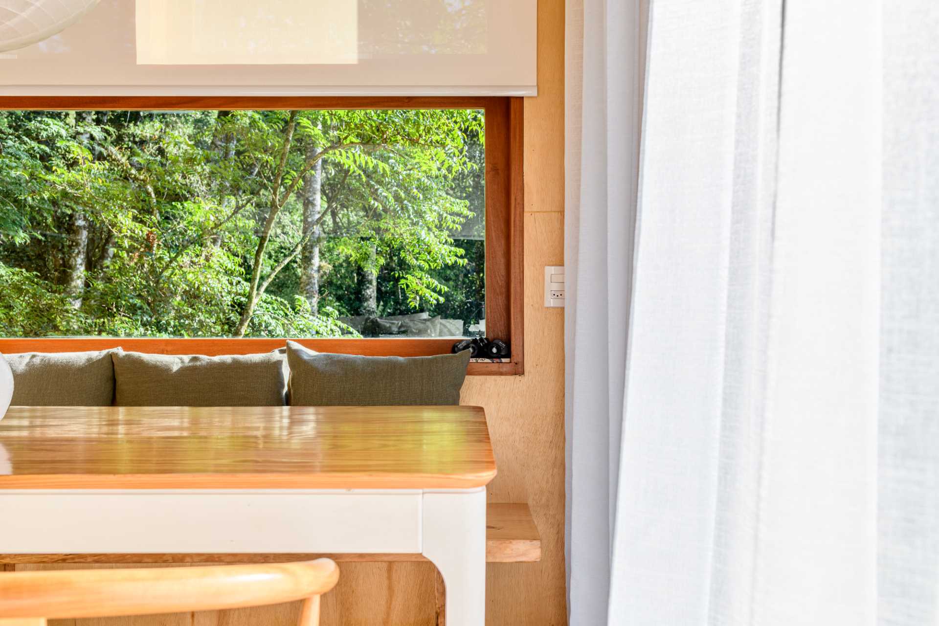 A modern tree house includes a dining area with a table and chairs, and a bench that runs underneath the window to the fireplace.