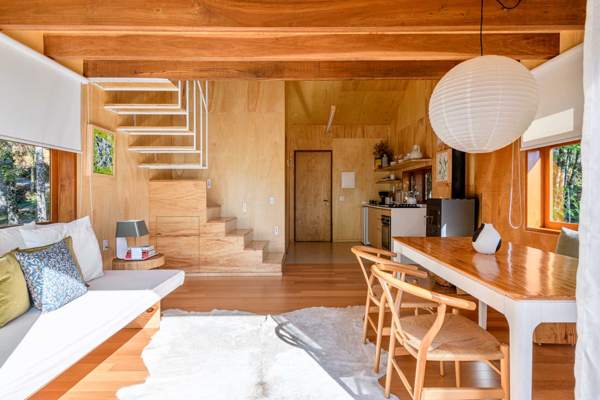 A modern tree house includes a dining area with a table and chairs, and a bench that runs underneath the window to the fireplace.