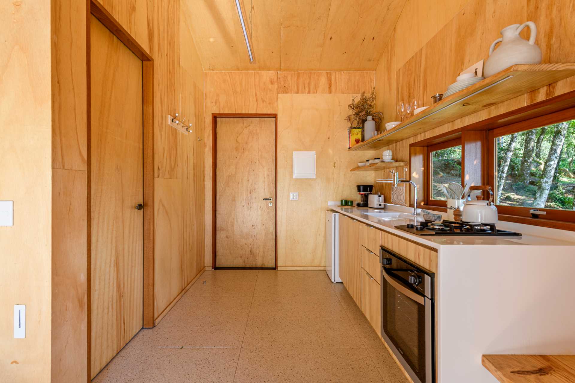 A modern tree house kitchen that includes wood cabinets, a white countertop, and floating shelves that provide additional storage.