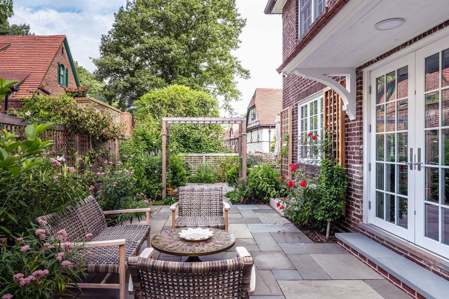 At the rear of this home, an overgrown patio was given a fresh look with new pavers, flowers, a fence, a seating area, and glass and wood patio doors.