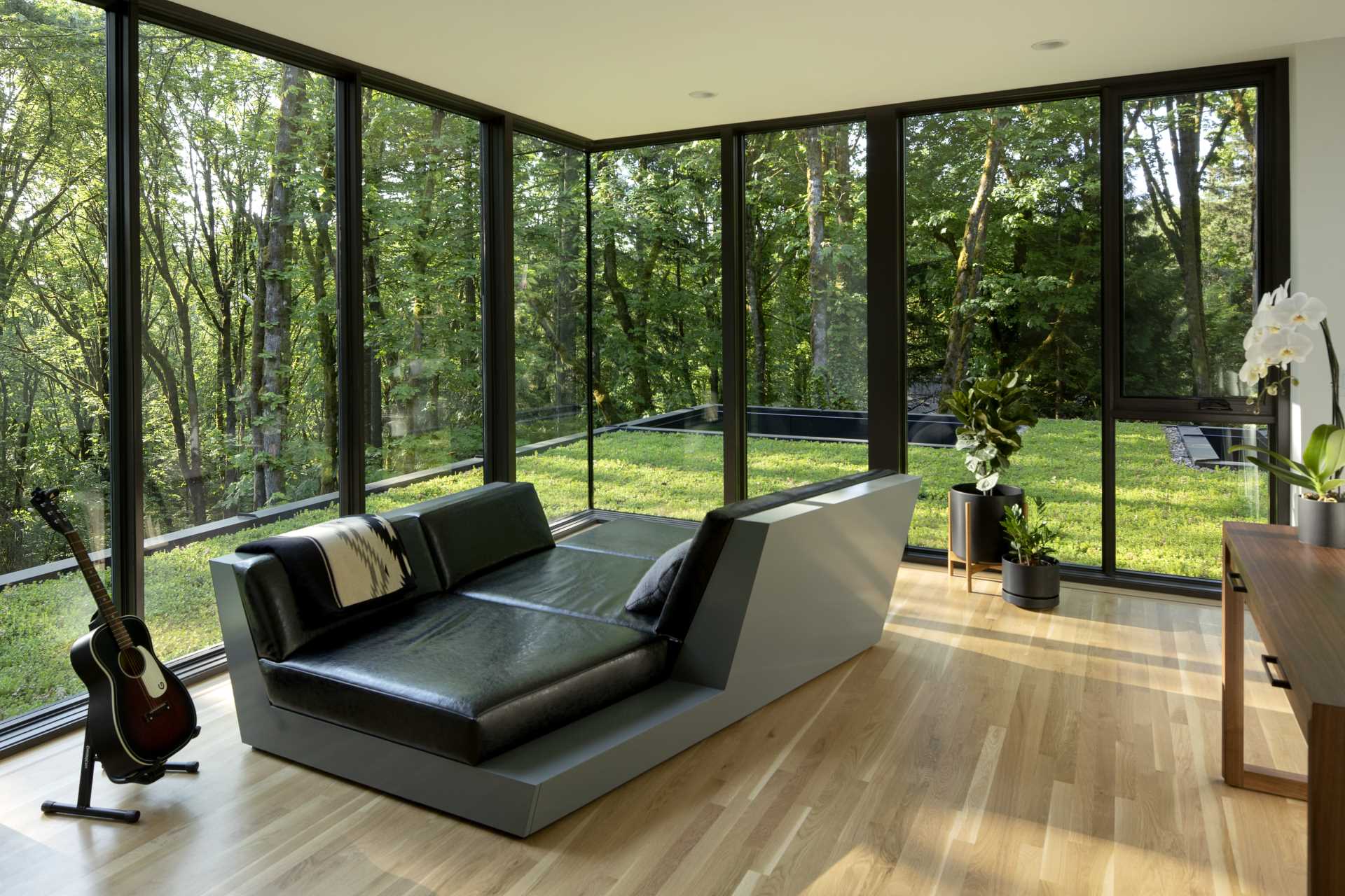 A modern sitting room with floor-to-ceiling windows that look out to a green roof and forest.