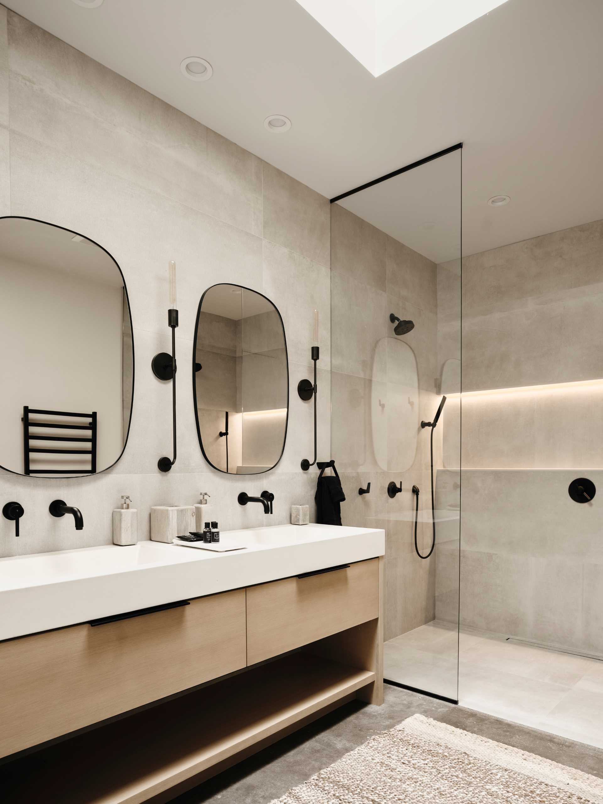 A bathroom with a neutral color palette with black accents and a skylight.