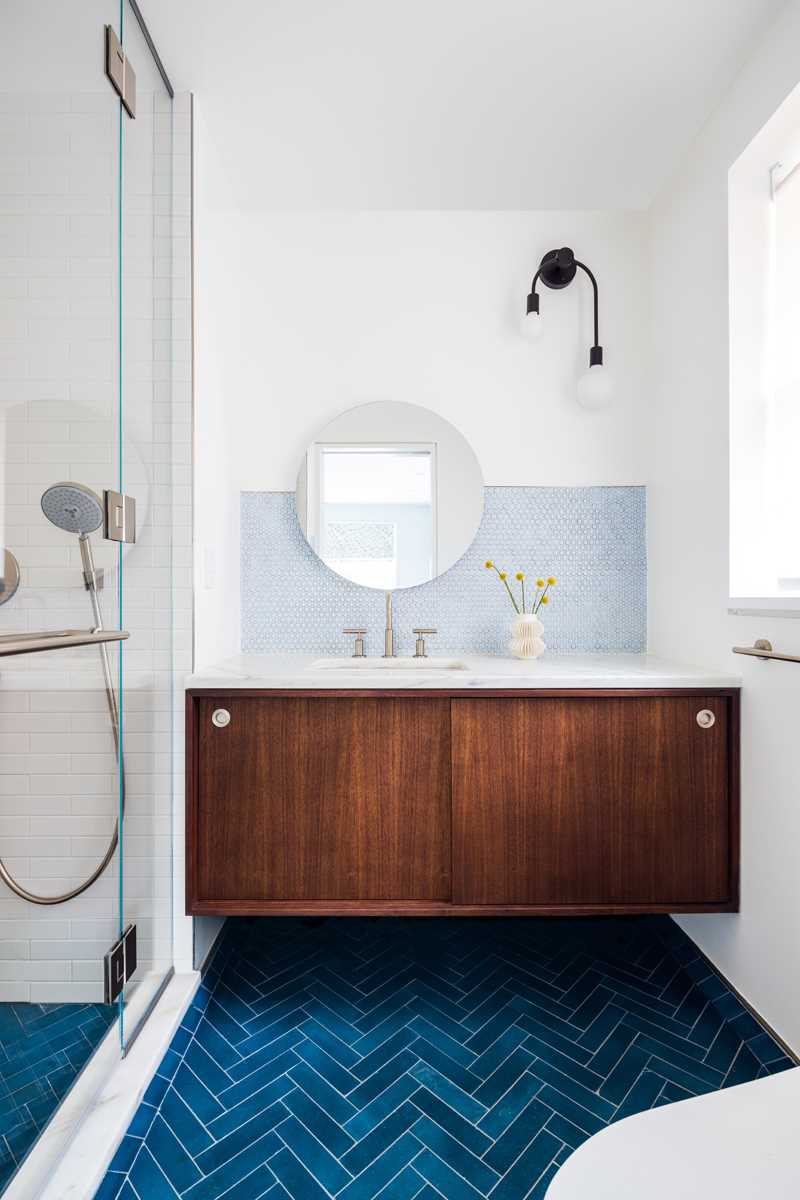 In this bathroom, a pale blue accent provides a backdrop for the round mirror, while the tiled floor is a much bolder blue.